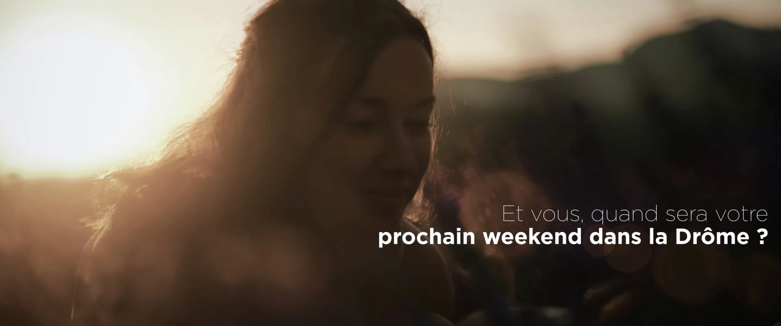 Une femme souriante regardant vers le bas, avec un coucher de soleil en arrière-plan et un texte en français demandant si vous souhaitez passer le prochain week-end en Drôme.