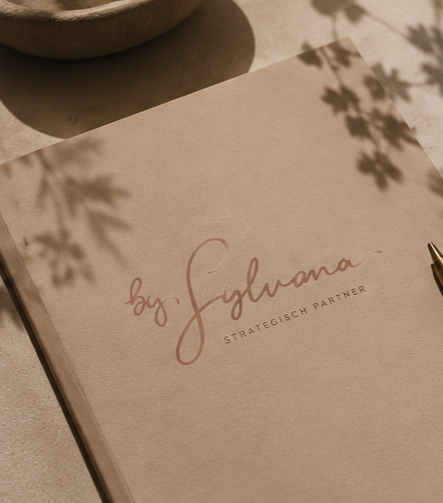 Beige notitieboek met By Sylvana logo op een minimalistische werkplek