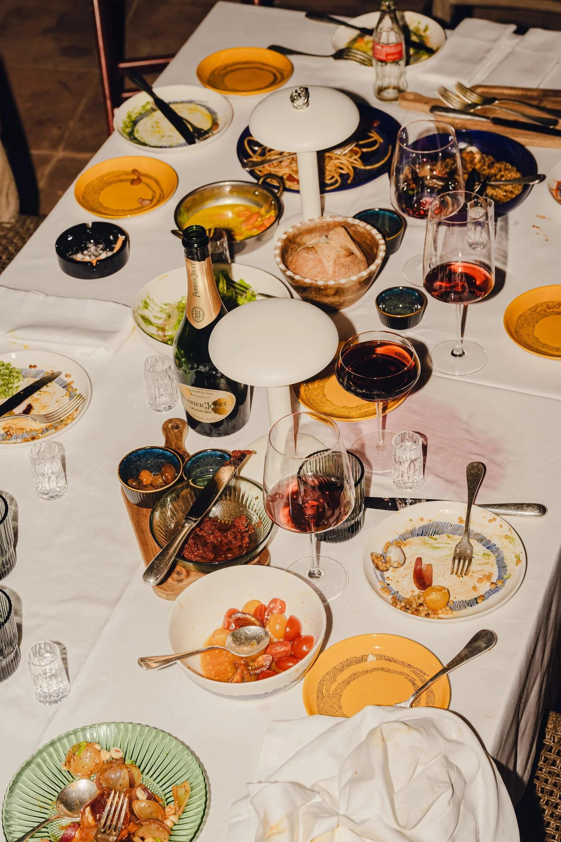 Ein gedeckter Esstisch mit leeren Tellern, leeren Gläsern, verschiedenen Resten und Essensresten, sowie einigen offenen Flaschen und Besteck, was auf eine zeremonielle Mahlzeit oder ein festliches Beisammensein hindeutet.