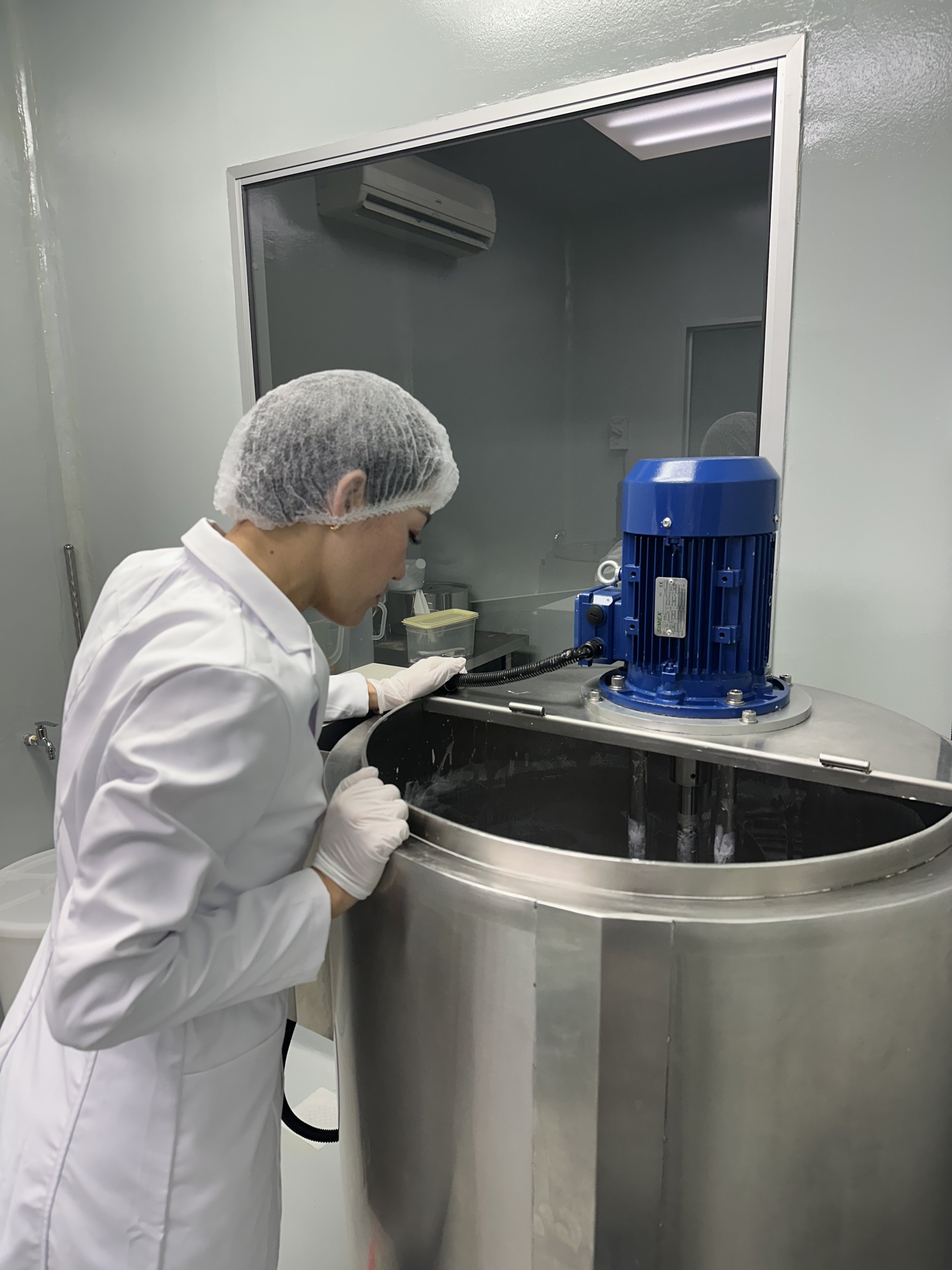 A woman in a white lab coat and hairnet working with a blue industrial machine in a sterile laboratory environment.
