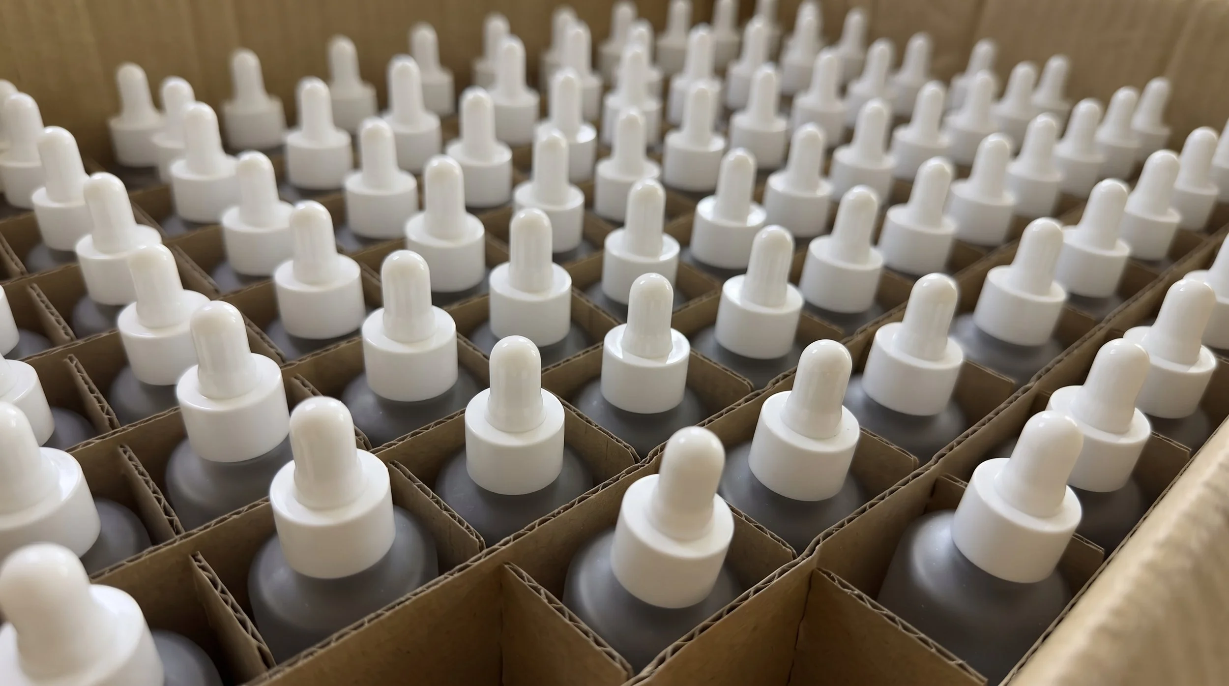 A close-up view of multiple white dropper bottles organized in cardboard compartments inside a box.