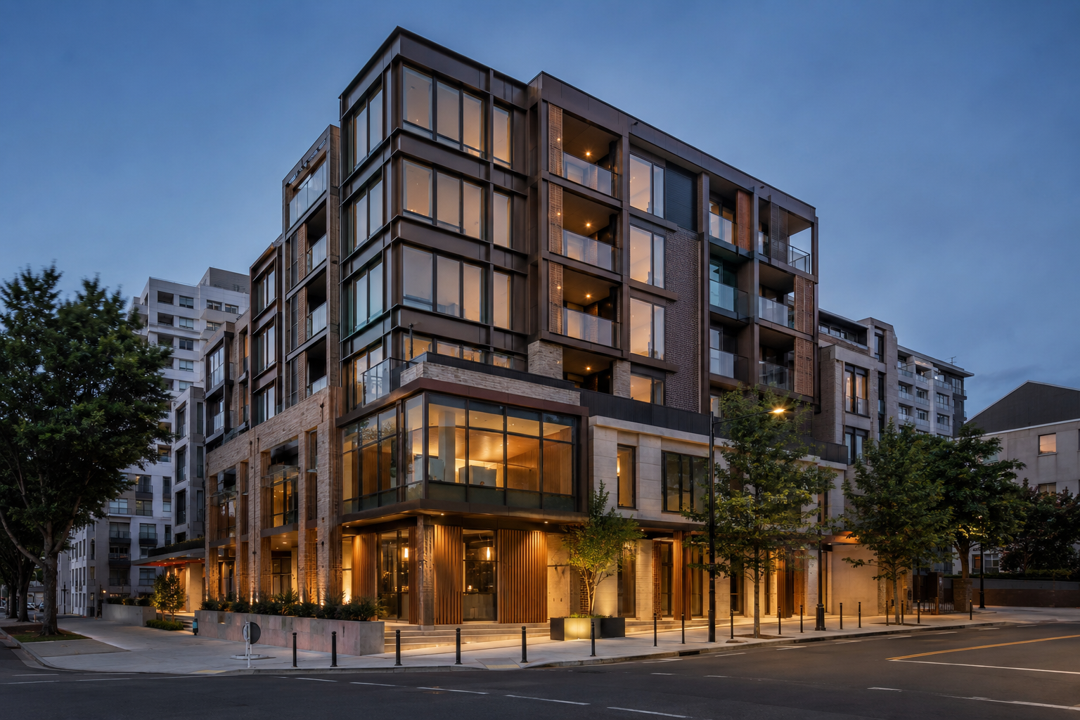 Modern multi-story apartment building at dusk with large glass windows, warm interior lighting, and street trees in front.