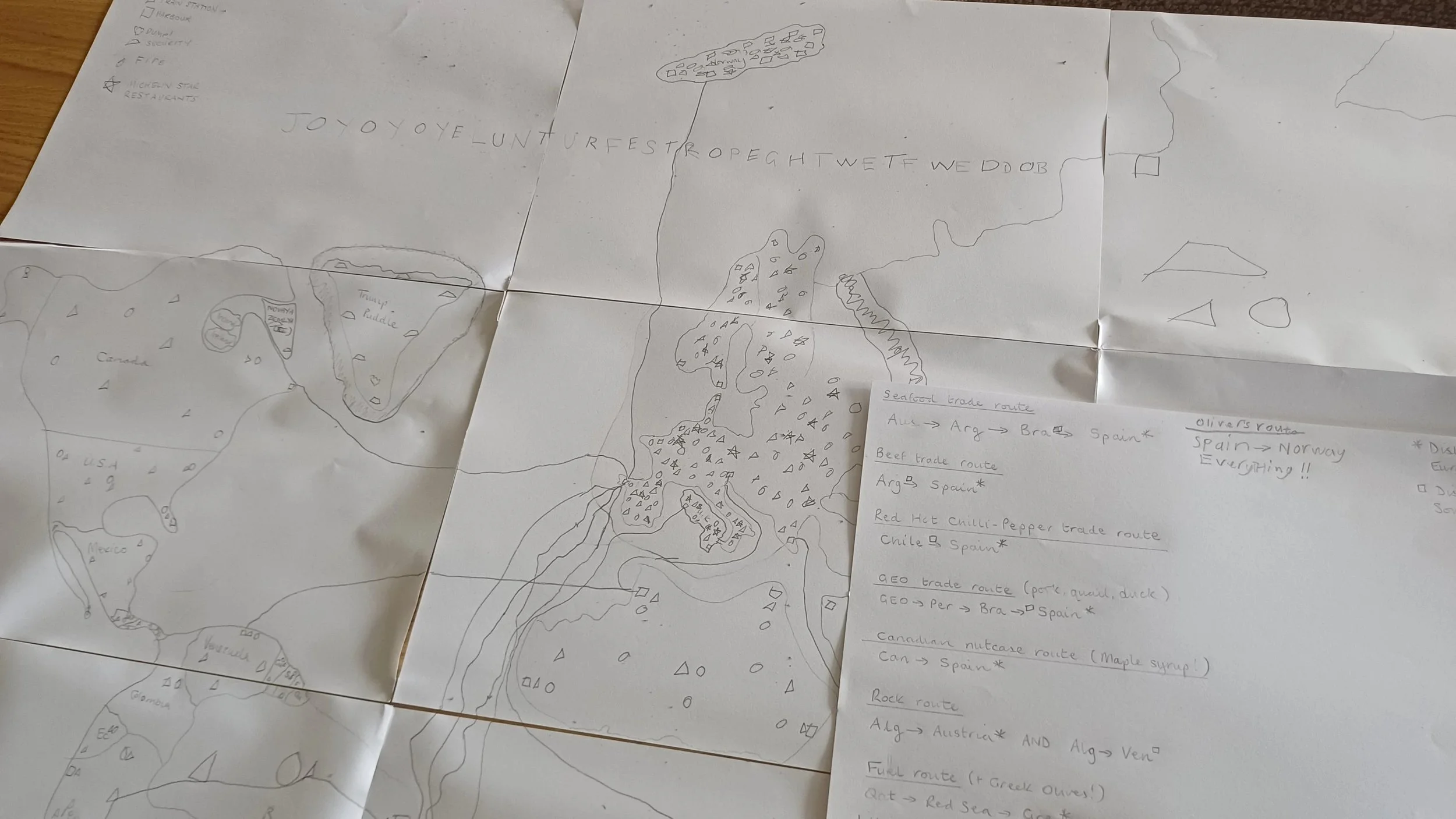 A hand-drawn map on several sheets of paper showing routes and regions, with labels such as 'season trade routes,' 'beer trade route,' and mentions of countries like Spain, Norway, and Chile. There are some sketches and notes about trade routes and regions, along with a small map of a landmass.