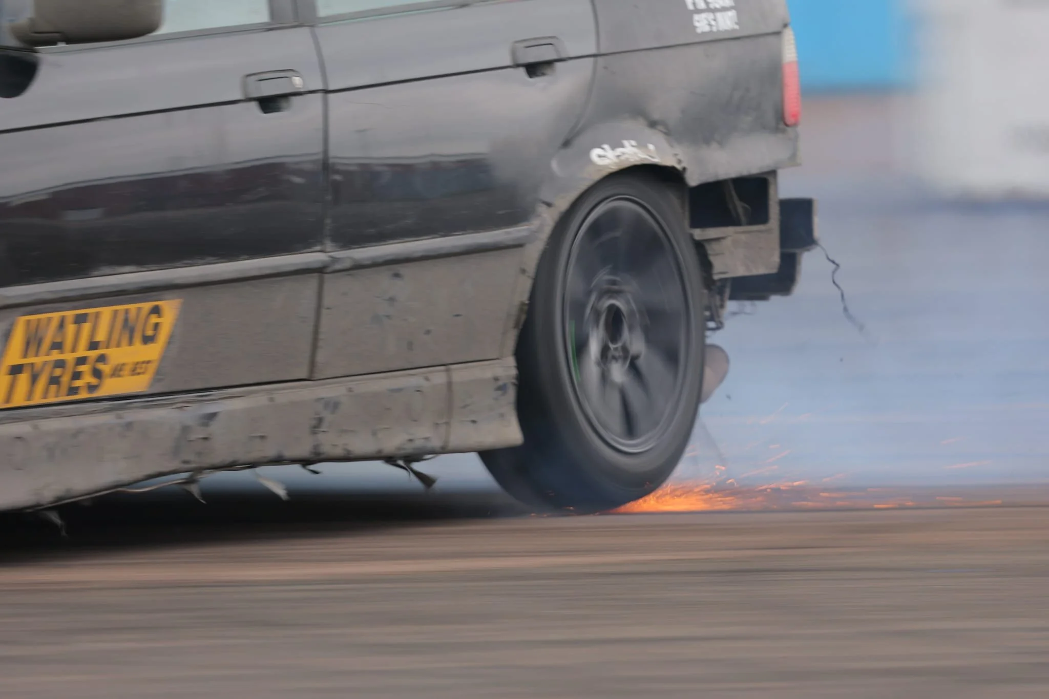 A black drift car driving at high speed making flames from the rear tyres
