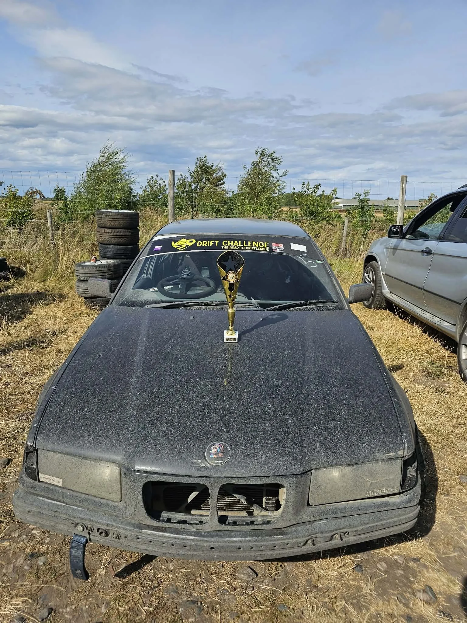 A dusty, black drift car with a second place drift trophy on its bonnet