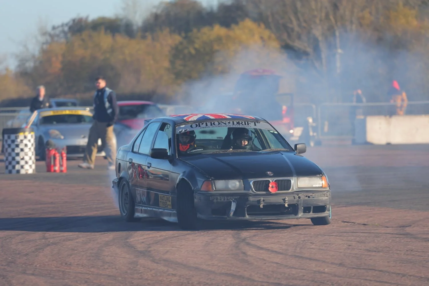 A black drift car blowing out smoke on track.