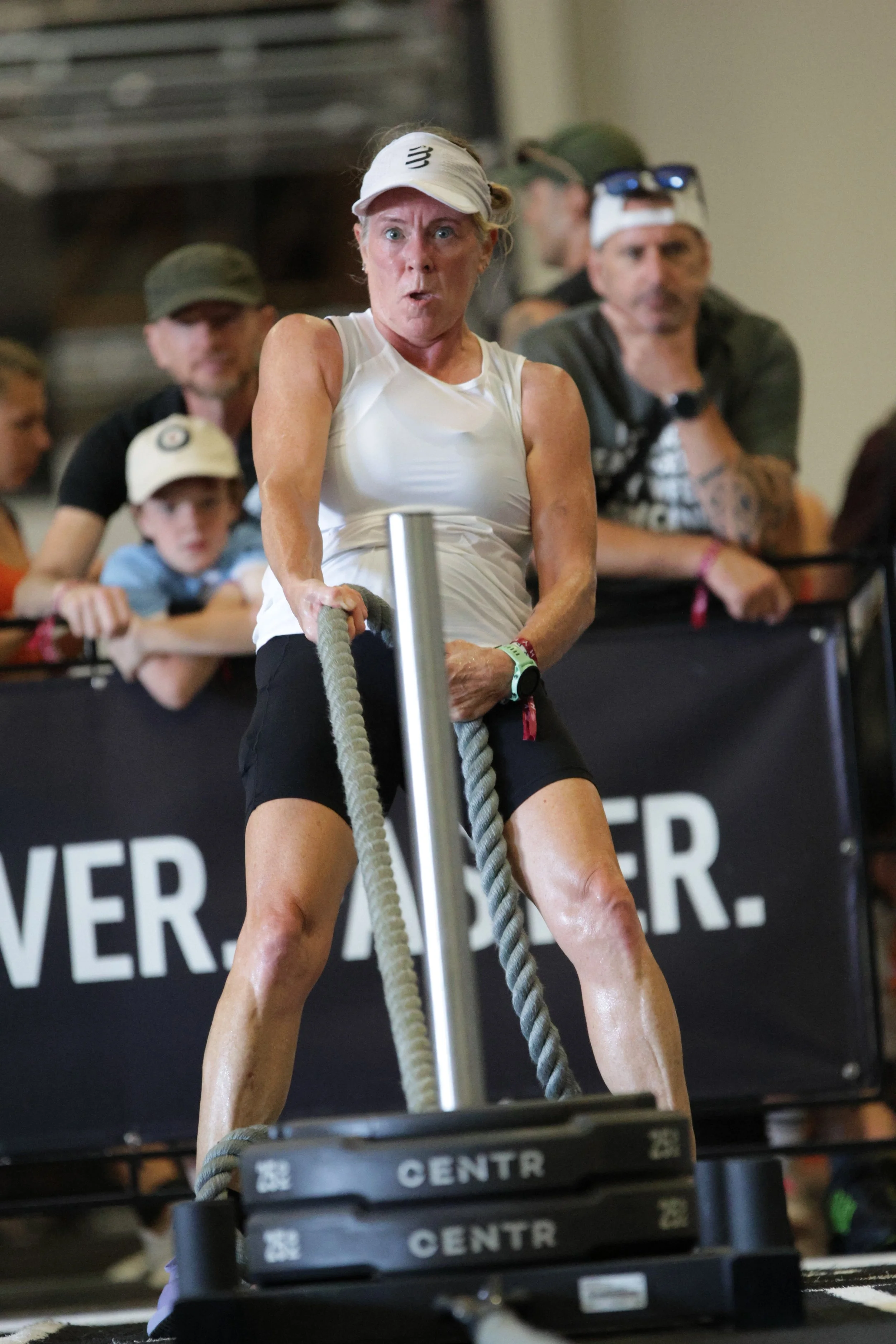Woman engaged in a tire flip workout at an indoor fitness event, with spectators watching behind her.