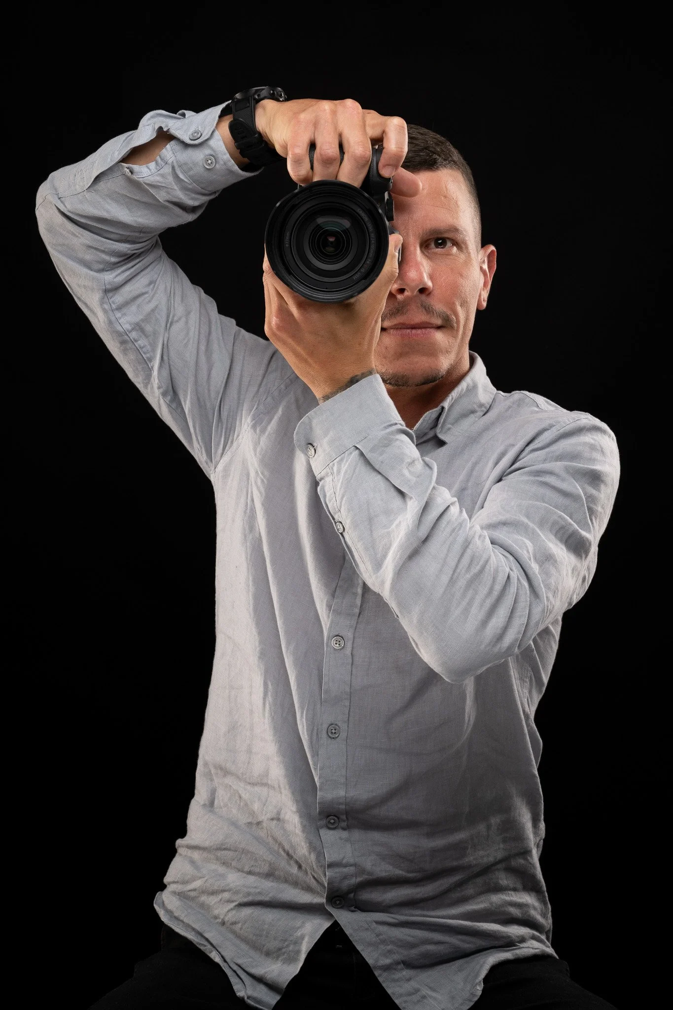 Person with short brown hair taking a photograph with a professional camera against a black background.