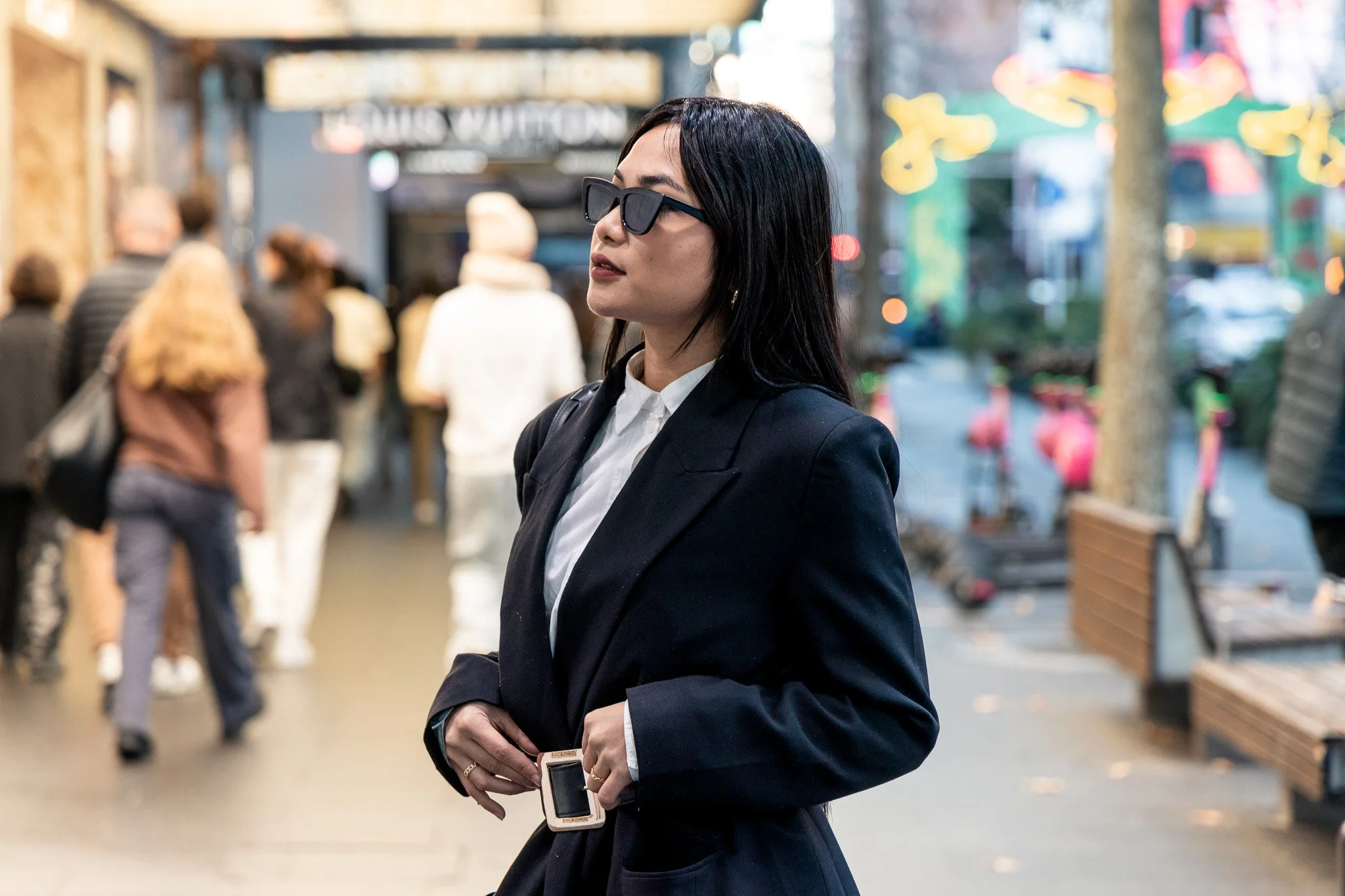Woman in professional suit wearing sunglasses in an outdoor shopping area.