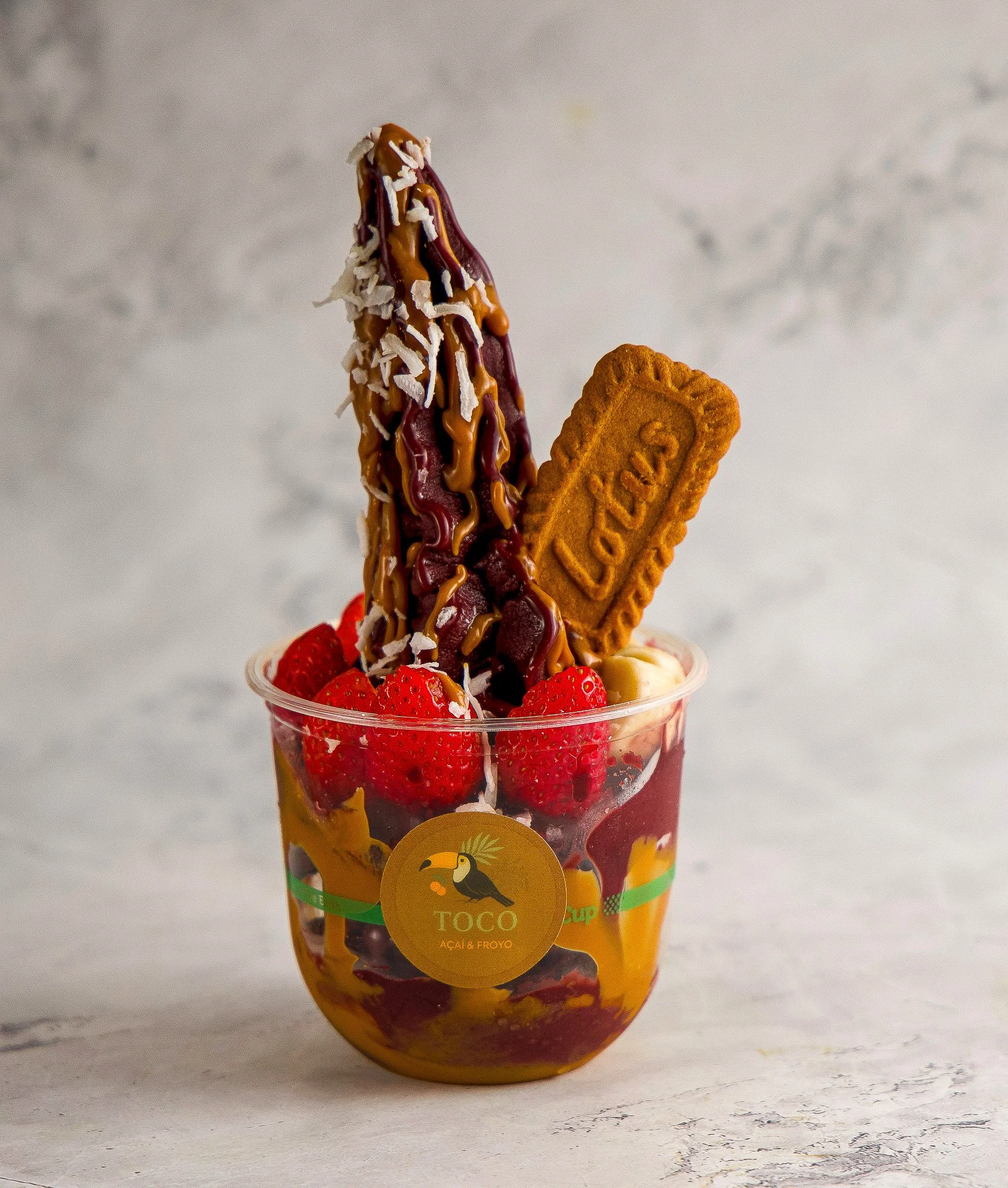 A cup filled with strawberries, banana slices, and other fruits topped with a sundae cone dipped in chocolate and drizzled with caramel and white chocolate.