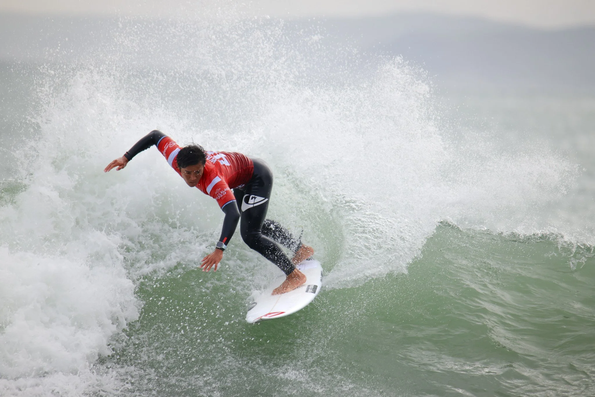 A male surfer in a red and black wetsuit riding a wave on a surfboard.