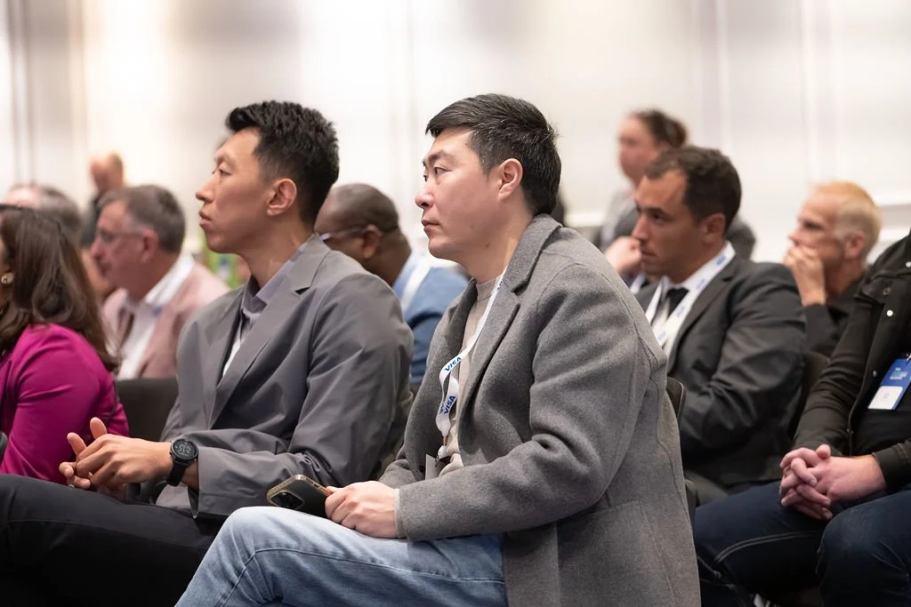 People attending a conference, seated in rows, listening attentively.