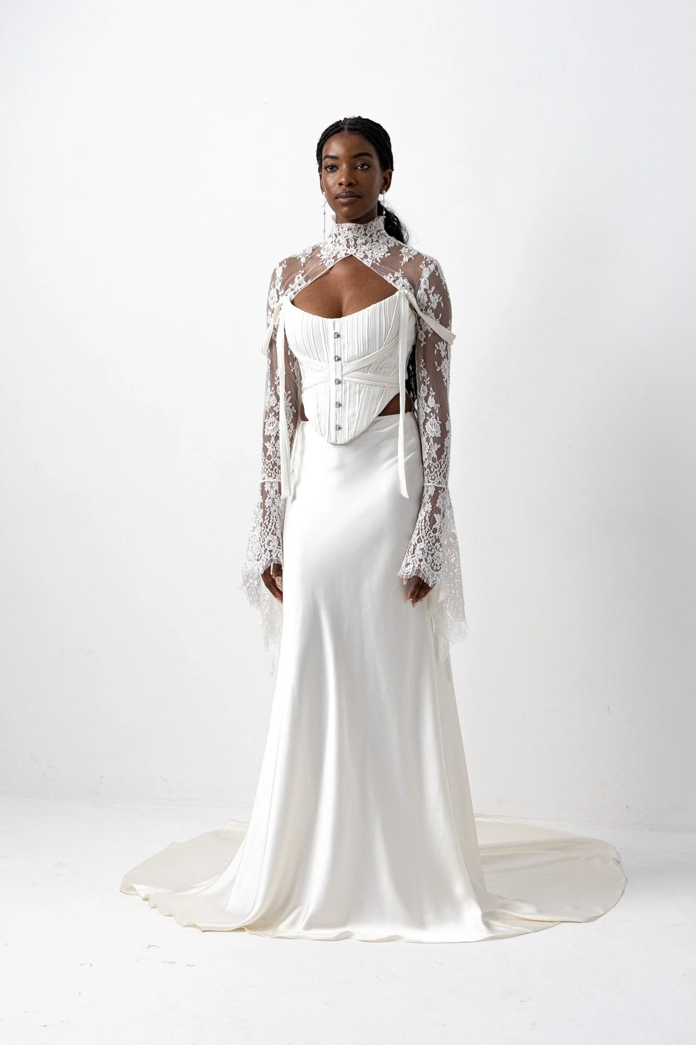 A woman in an elegant white wedding dress with a high lace collar and lace sleeves, standing against a plain white background.