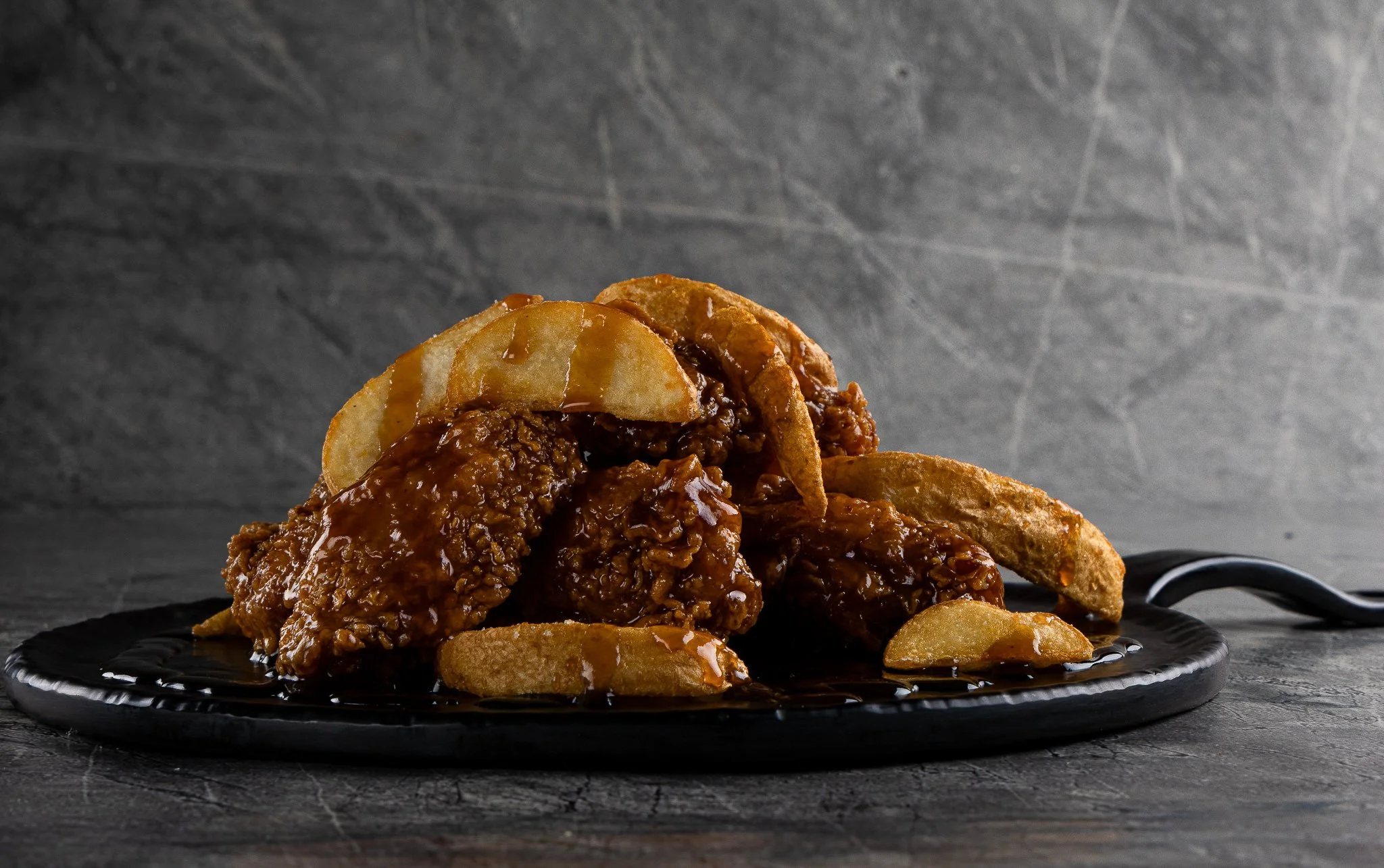 A close-up of barbecue ribs topped with sauce, with potato chips on a black plate on a dark surface.