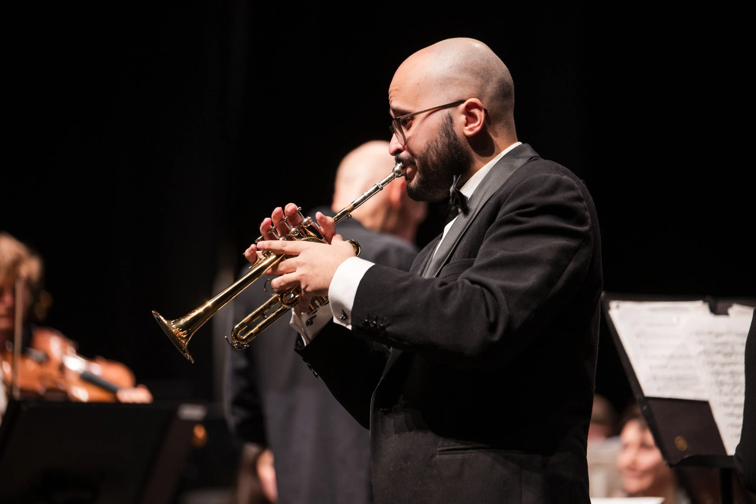 Man in tuxedo playing a trumpet during an orchestra performance.