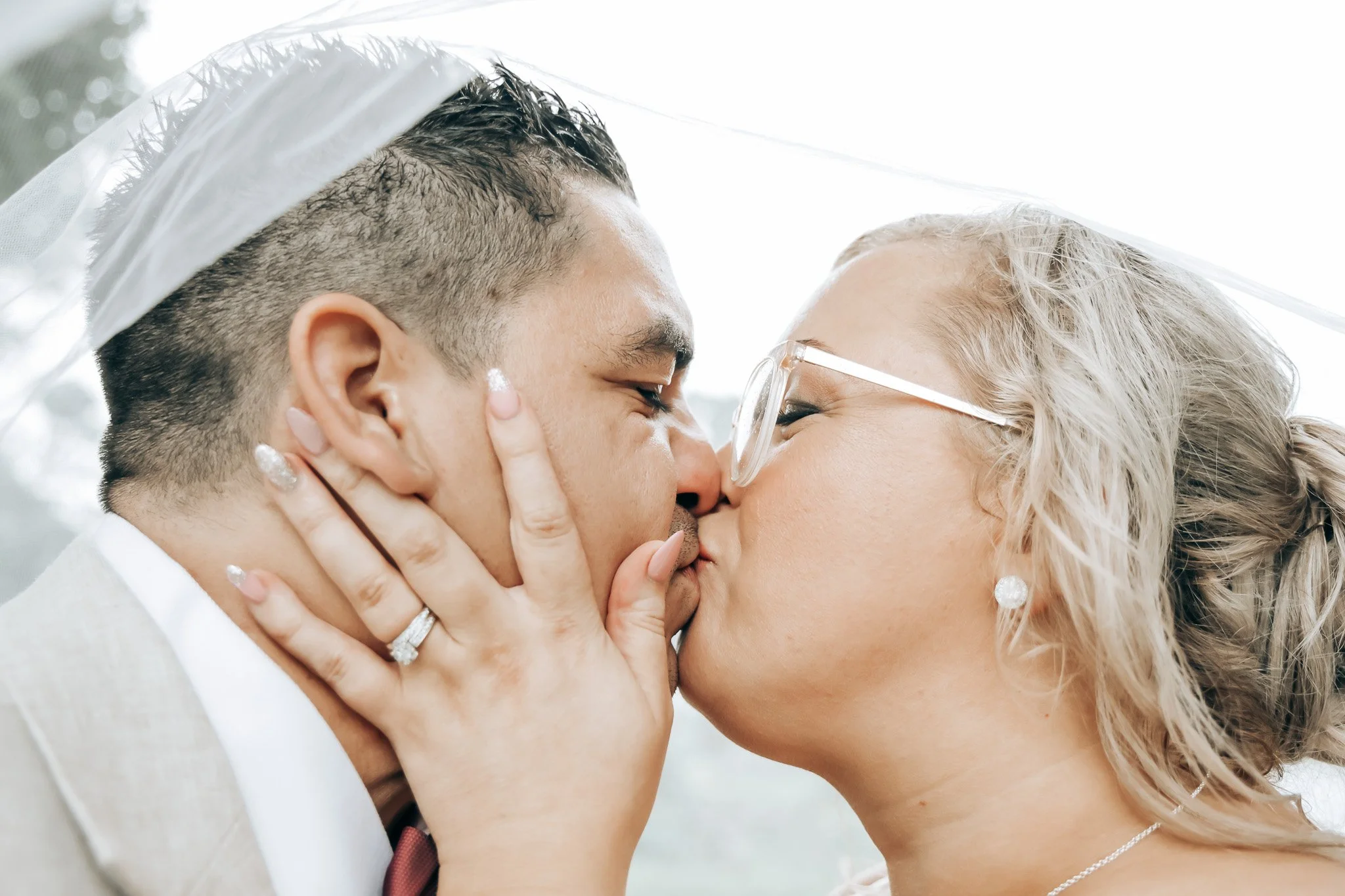 A couple sharing a close, intimate kiss, with their eyes closed and hands gently touching each other's faces, during a wedding celebration.