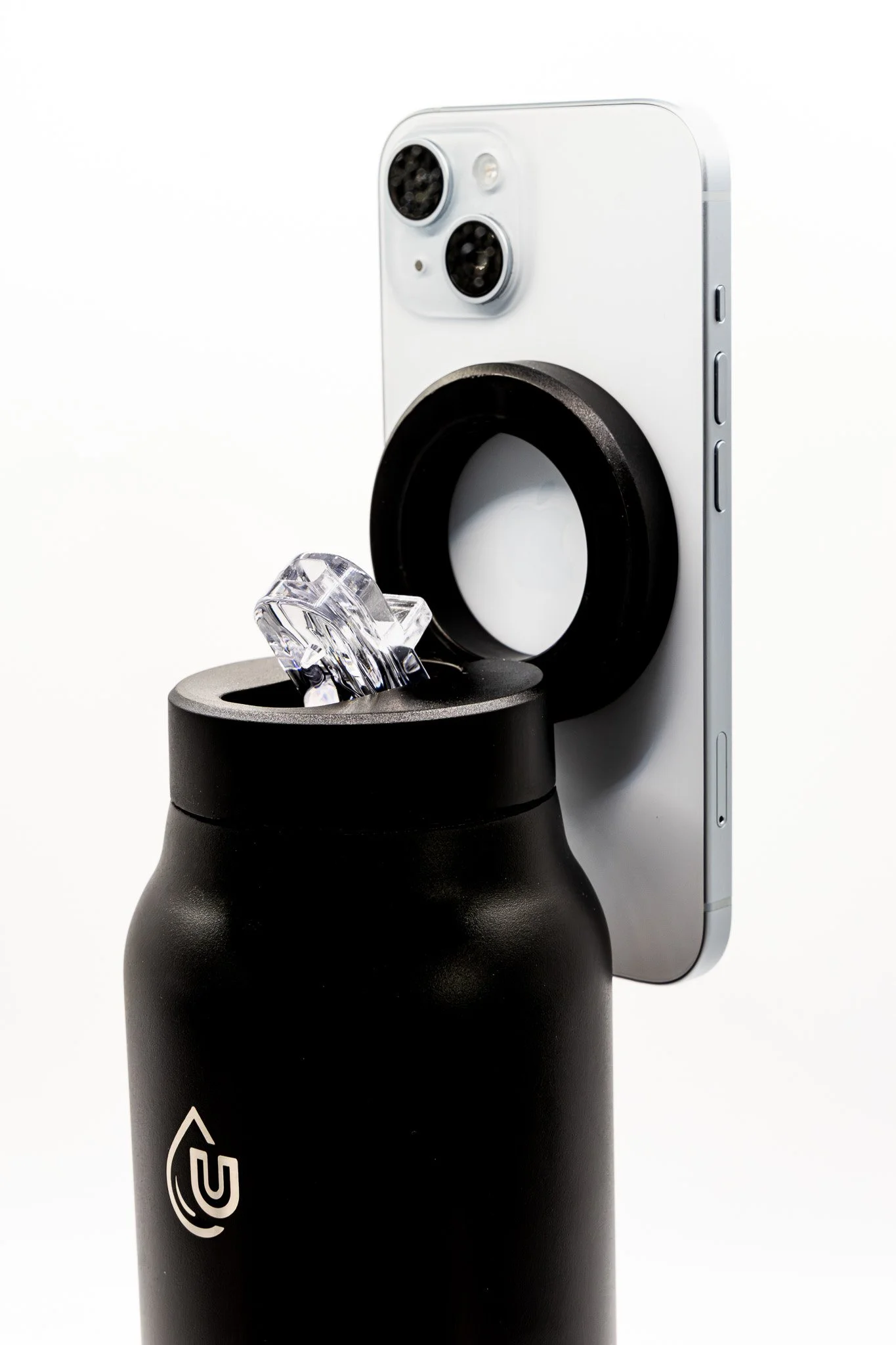 Smartphone placed onto a black bottle with a clear ice crystal on top, set against a plain white background.