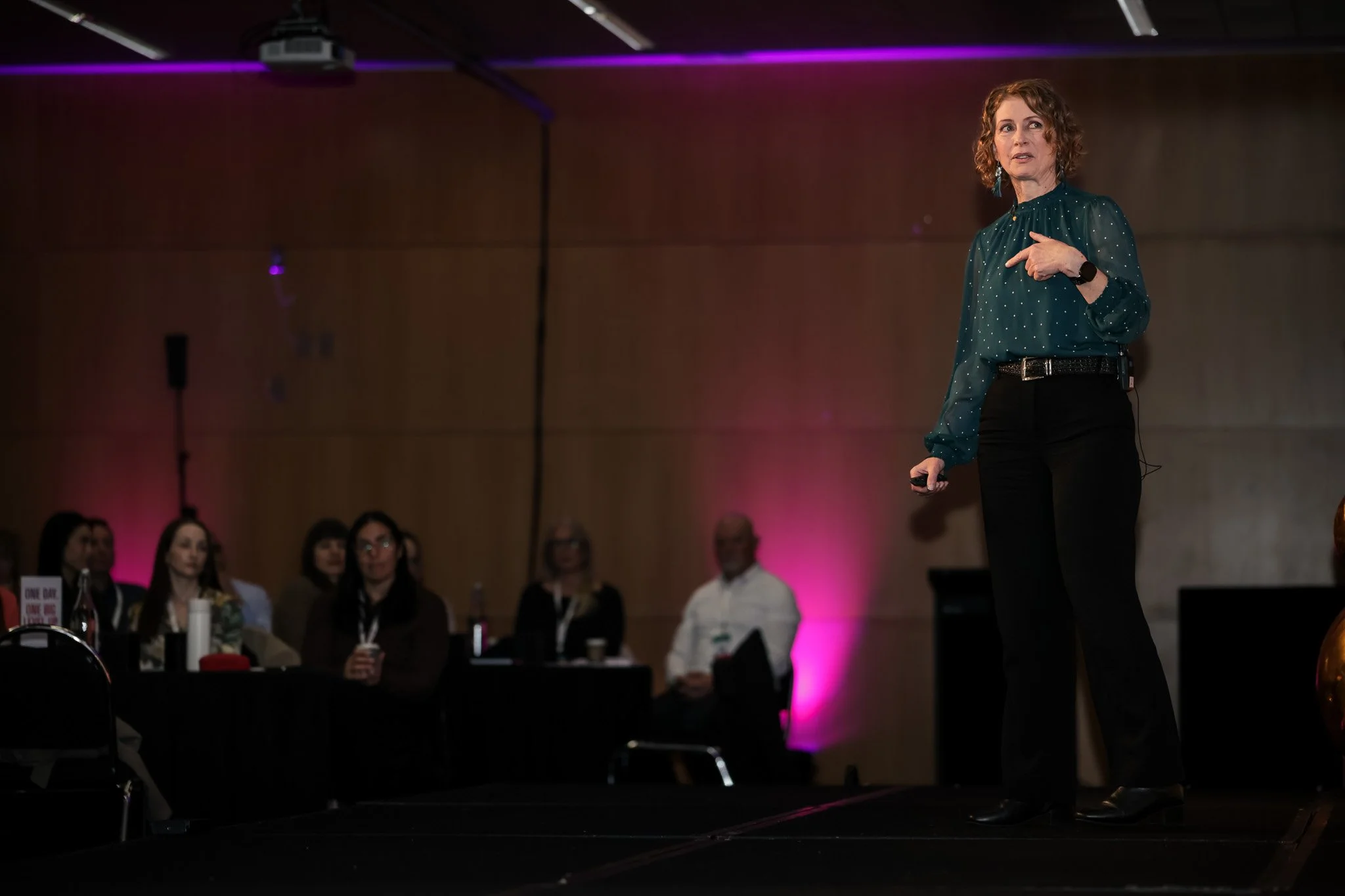 A woman giving a presentation or speech on a stage in front of an audience at a conference or event.