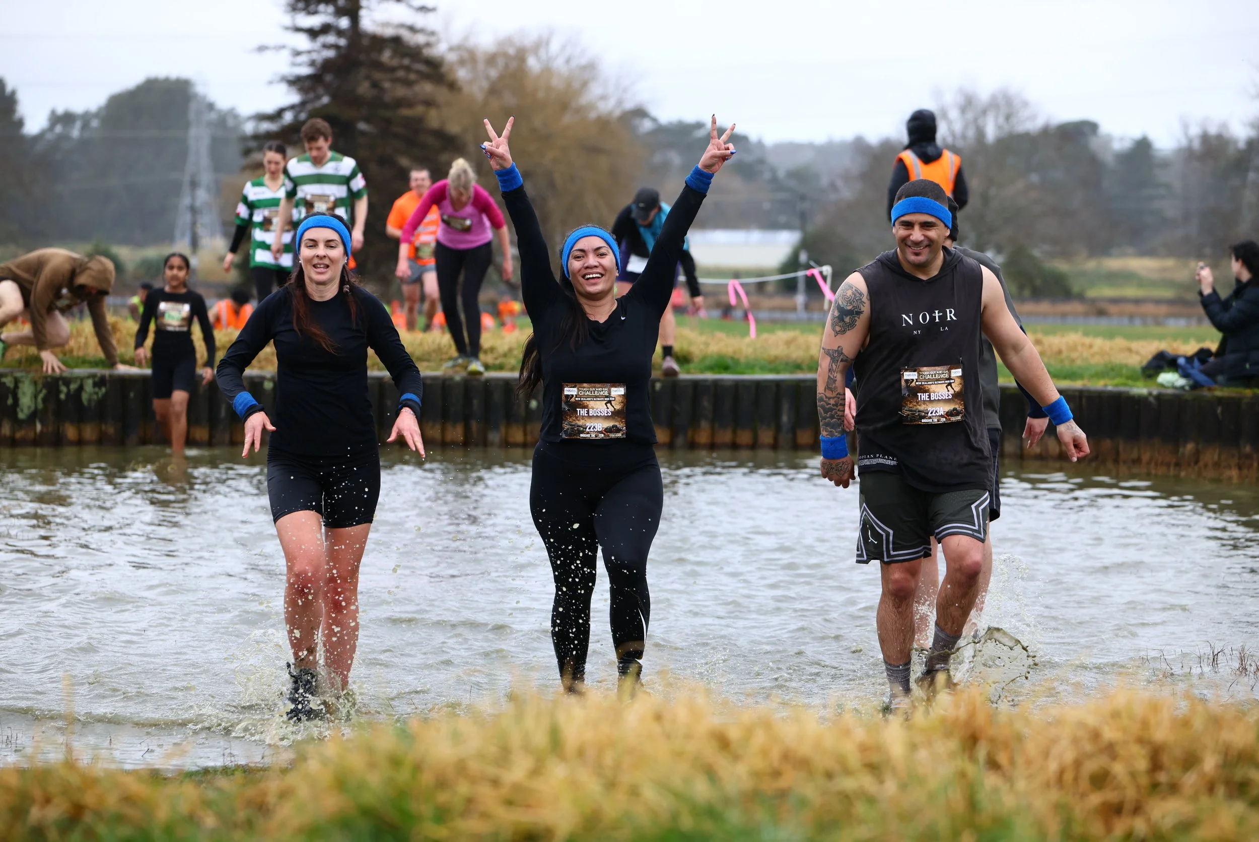 People participating in an outdoor obstacle course, crossing a body of water, often called a mud run or adventure race.