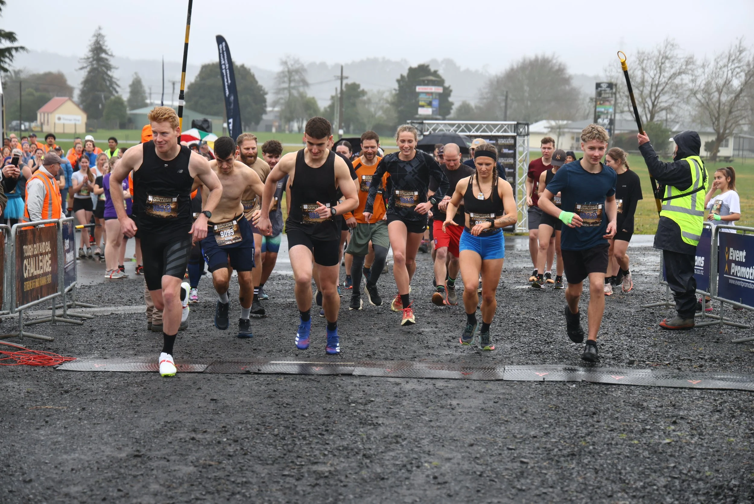 Group of runners participating in a race on a rainy day, with spectators and volunteers around them.