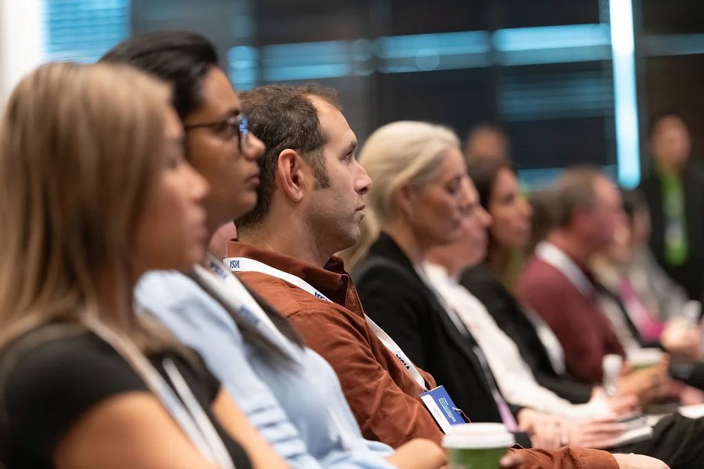 People attending a conference or seminar, sitting in rows, paying attention to a speaker or presentation.