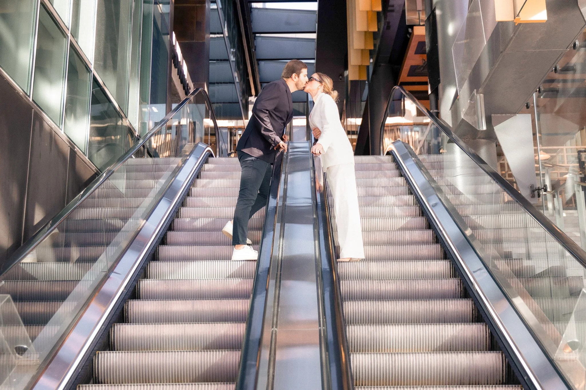 A man and woman sharing a kiss on an escalator in a modern building.