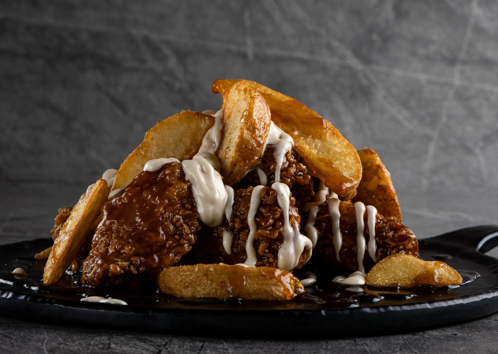 Close-up of a serving of loaded potato wedges topped with chili, melted cheese, and drizzled with sour cream on a black plate against a dark textured background.