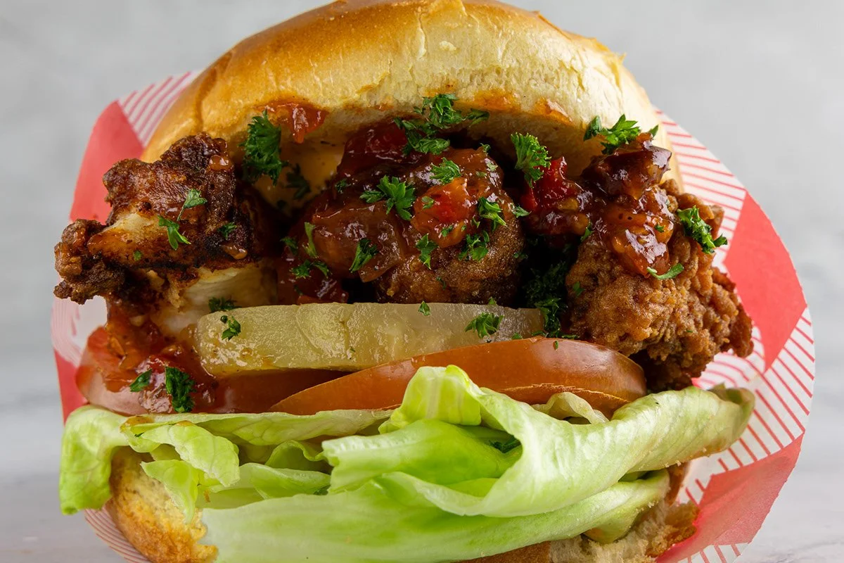 A fried chicken sandwich with lettuce, tomato, pickles, fried chicken, barbecue sauce, and a sandwich bun