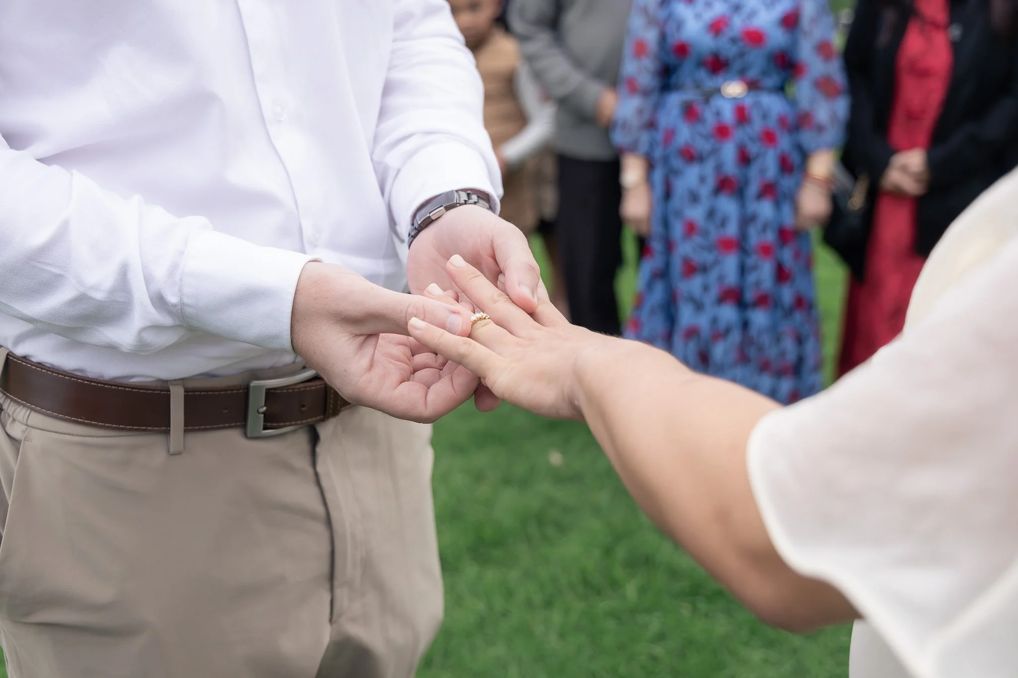 People exchanging rings during a wedding ceremony outdoors.