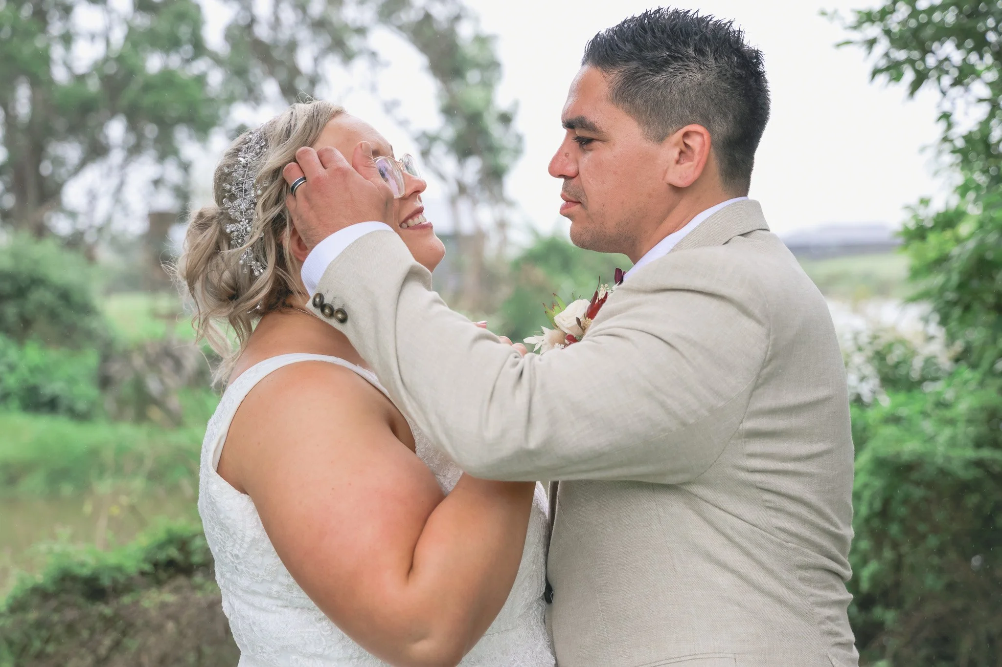 Bride and groom in wedding attire sharing an intimate moment outdoors surrounded by trees.