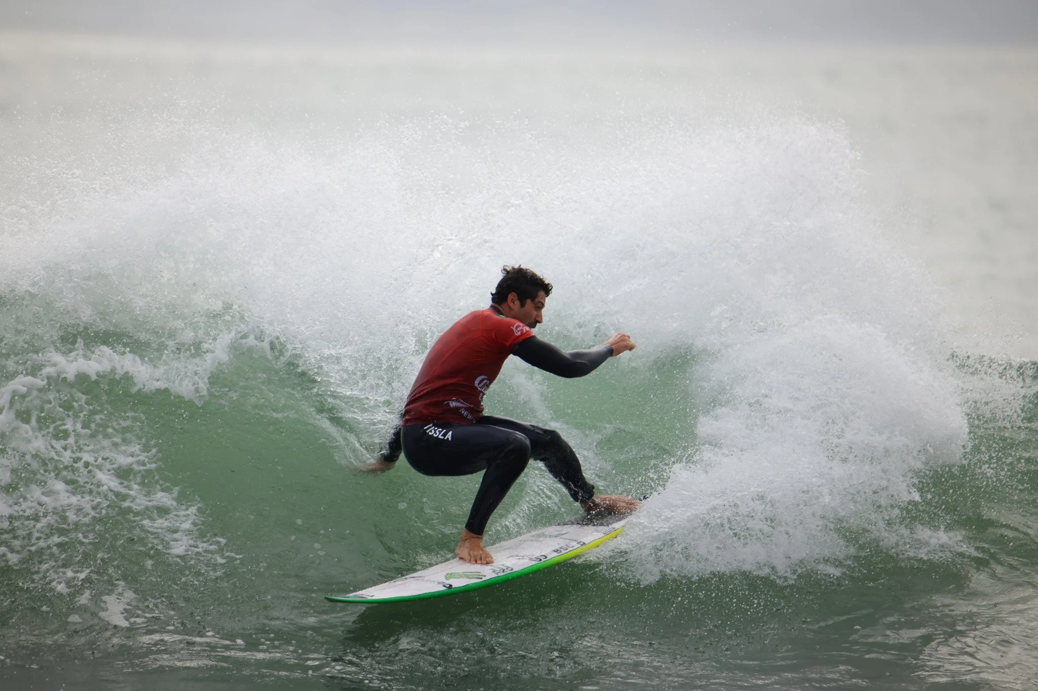 A male surfer wearing a red wetsuit riding a green surfboard on a wave in the ocean.