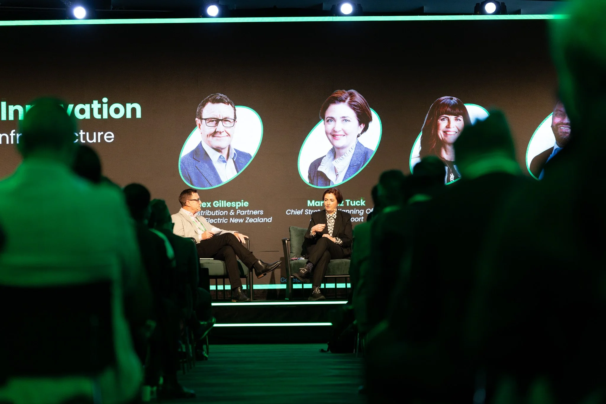 Panel discussion at a conference on innovation, featuring four speakers on stage with a large screen behind them showing their photos and names.