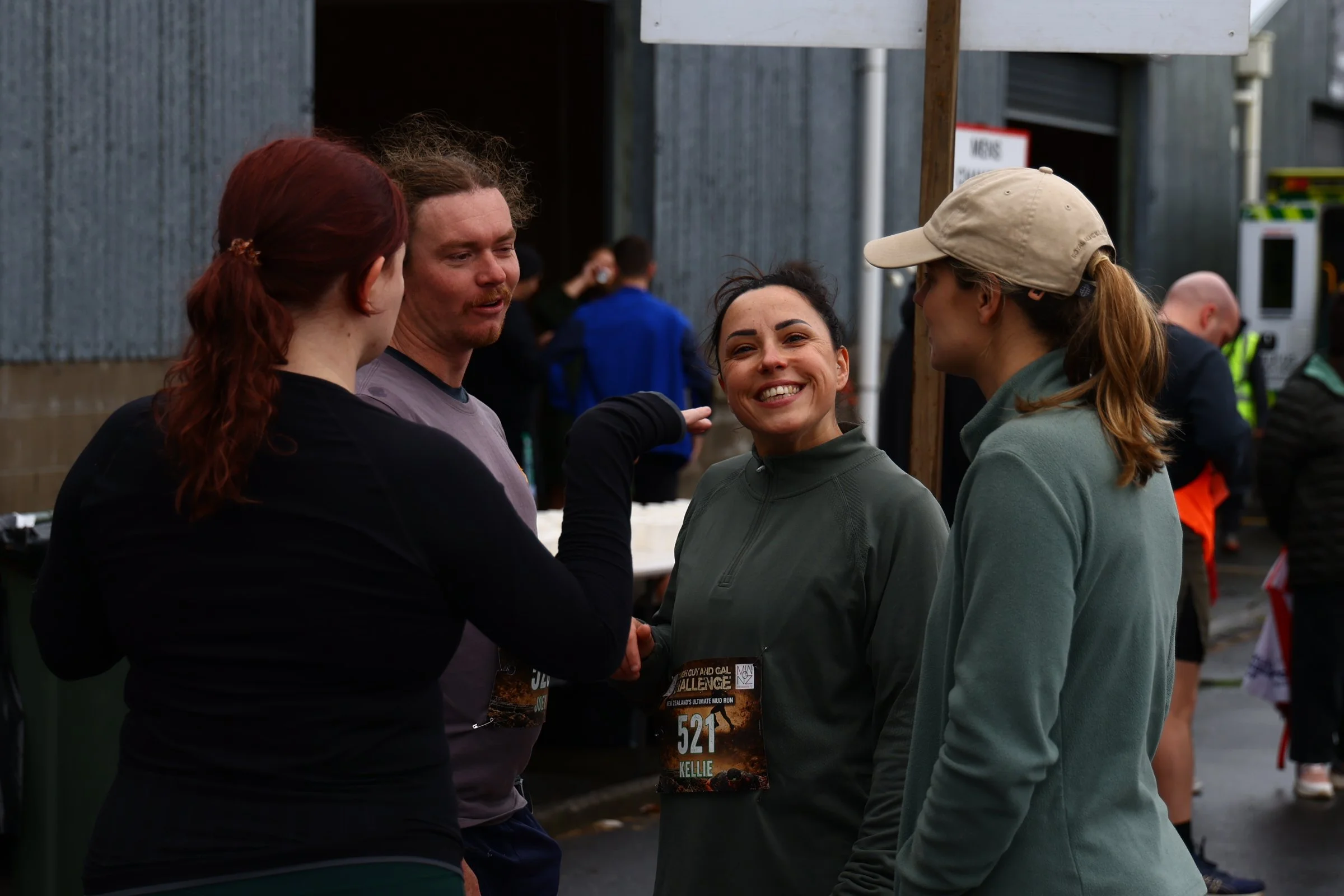 Four people standing in a group having a conversation outdoors. Three women and one man, with people and event banners in the background.