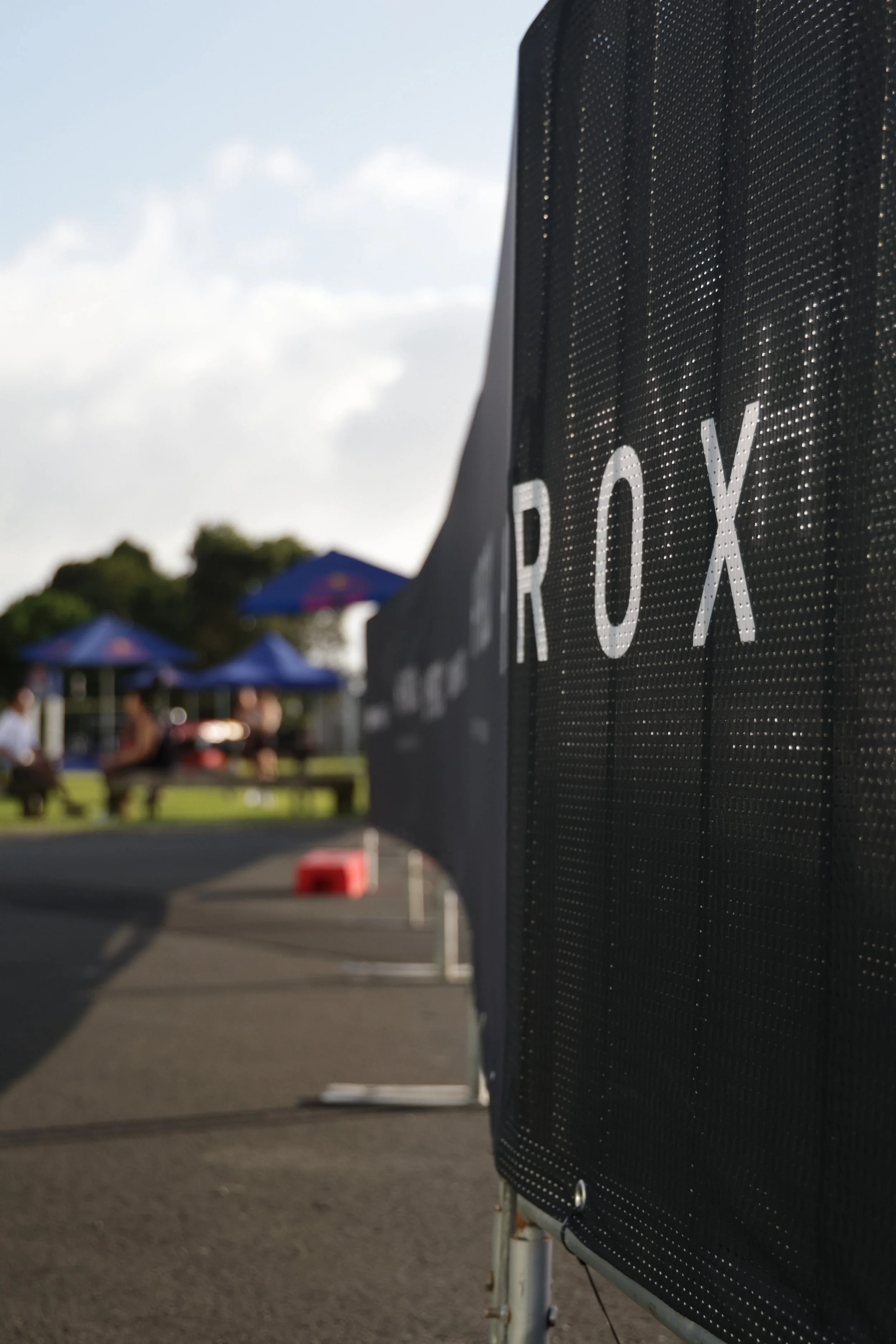 Parking lot with blue umbrellas and trees in the background, focus on an electronic billboard with partially visible text 'ROX' in the foreground.