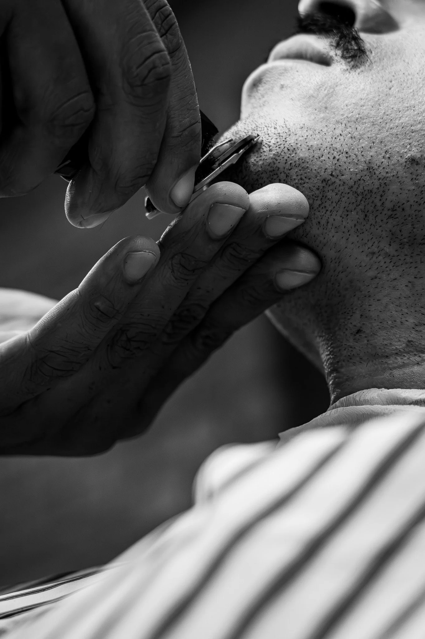 Close-up of a man getting a shave with an electric razor, focusing on his face and hand, with a striped shirt cuff visible.