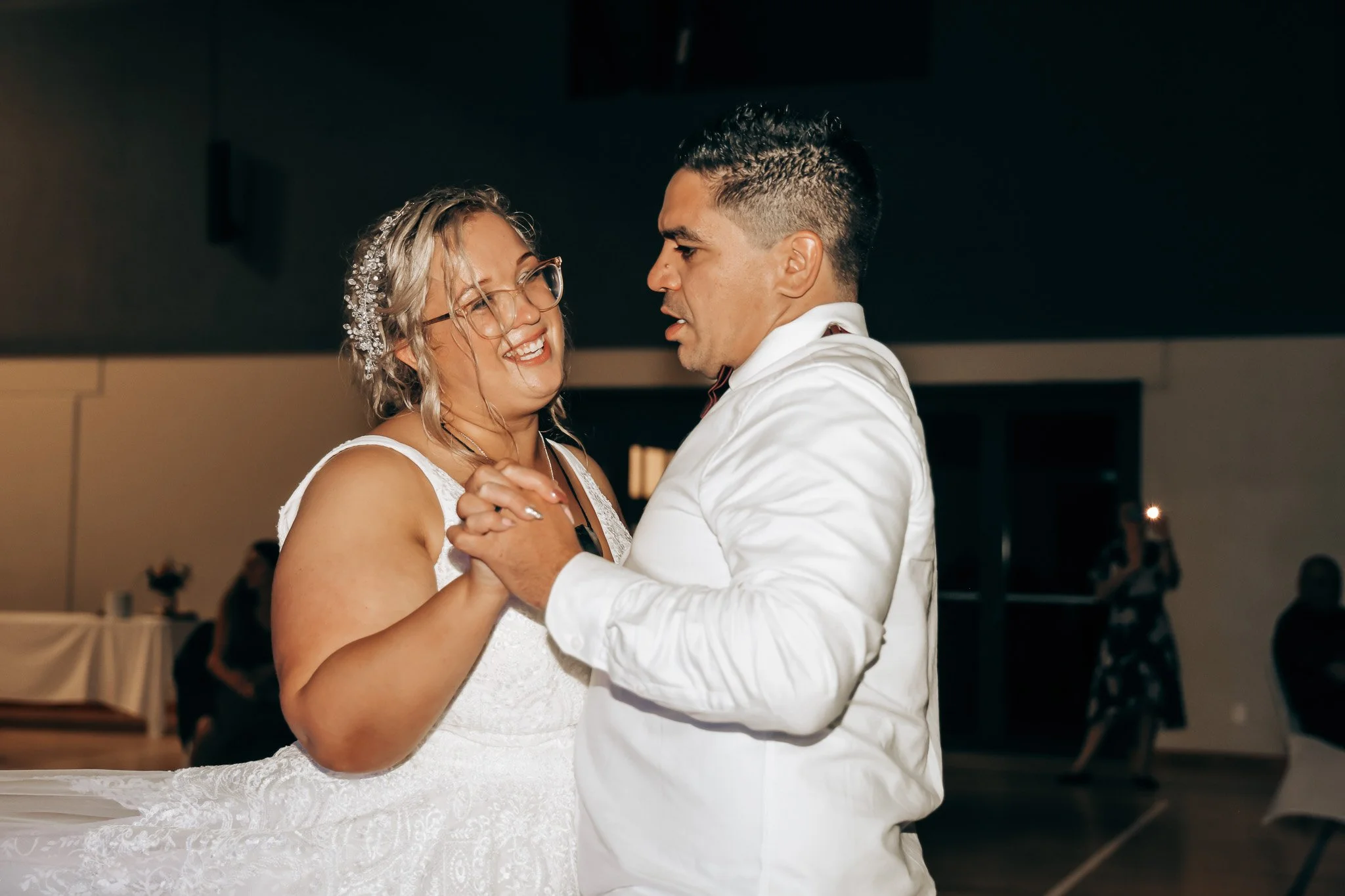 A bride and groom share a dance at their wedding reception, holding hands and looking at each other with smiles.