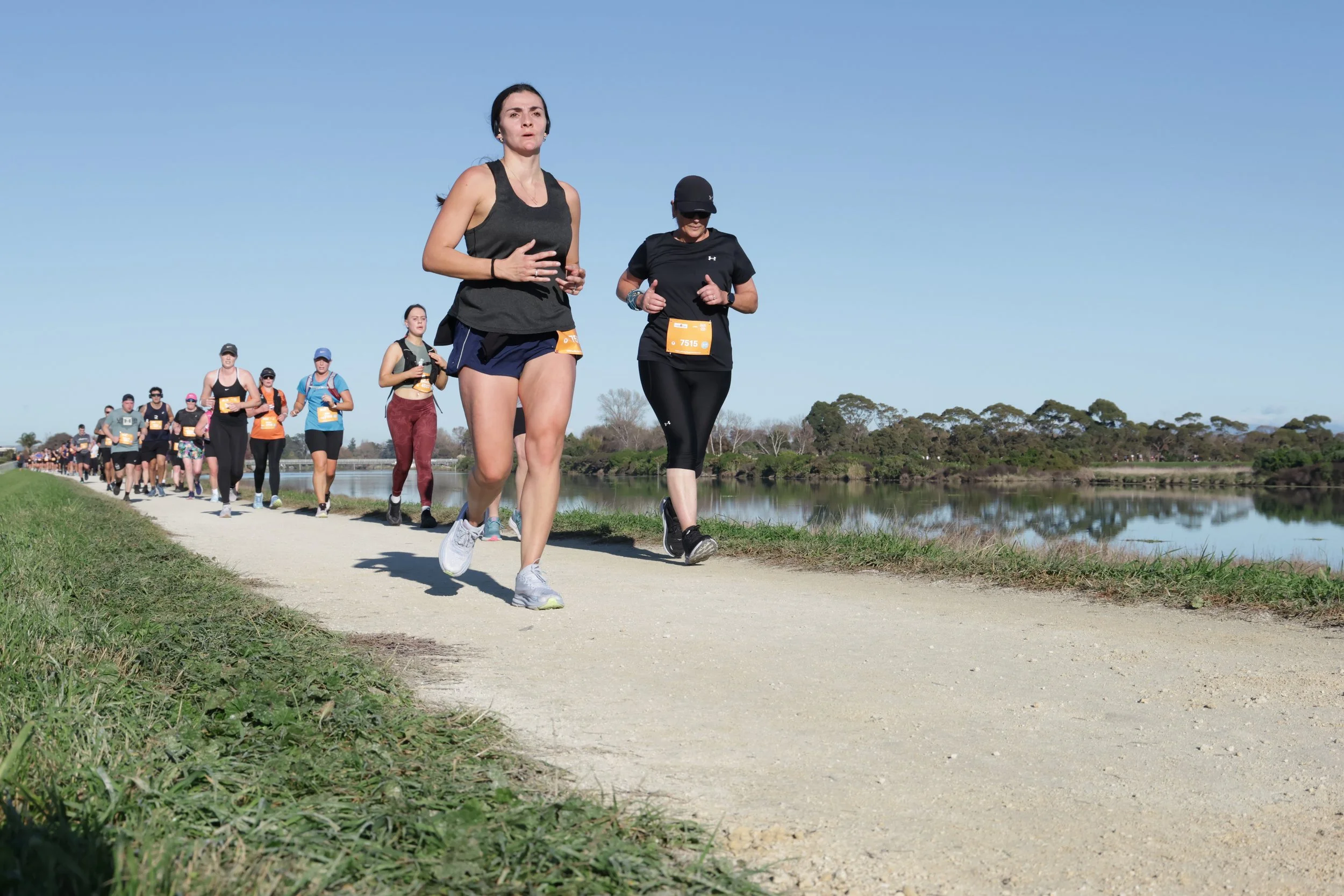 Group of people participating in a running event along a scenic trail by a river on a clear day.
