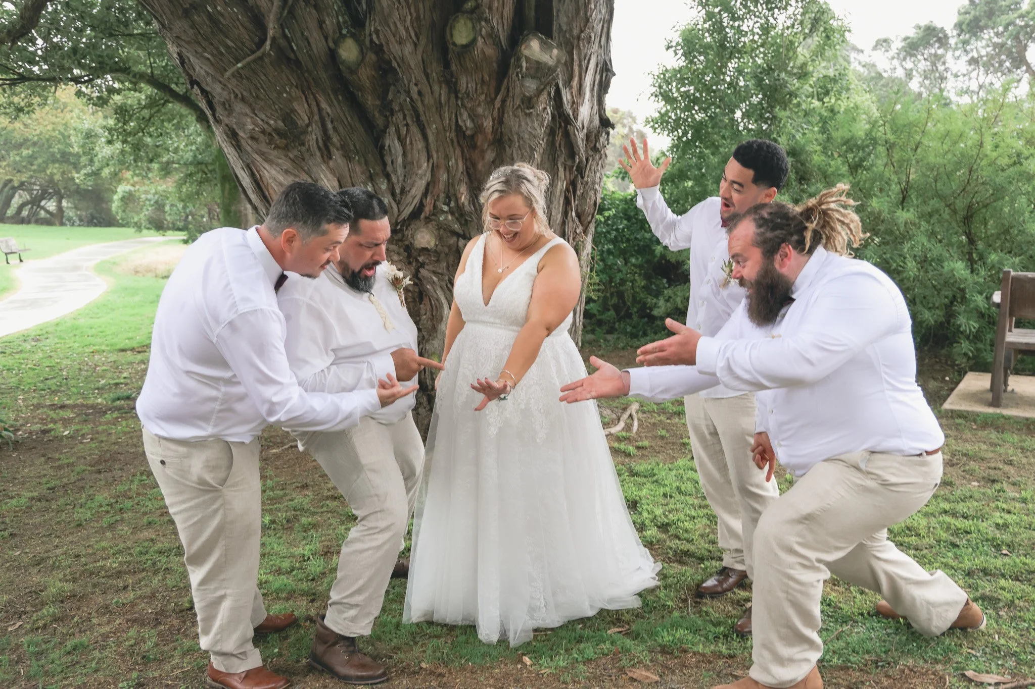 A group of five people, four men and one woman, dressed in white, standing outdoors near a large tree, appearing to celebrate or have fun together.