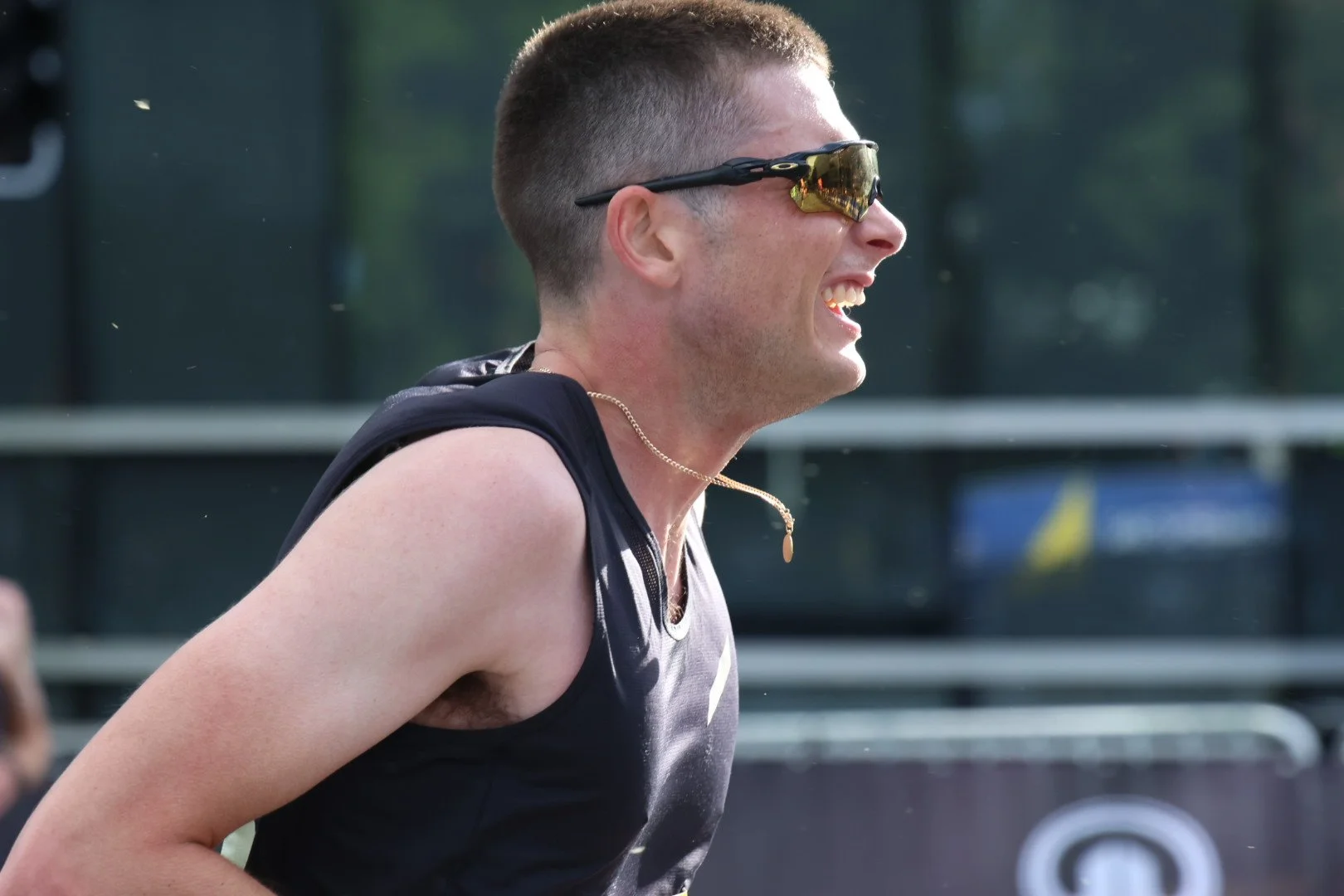 A man with short hair and sunglasses smiling during a sports event.