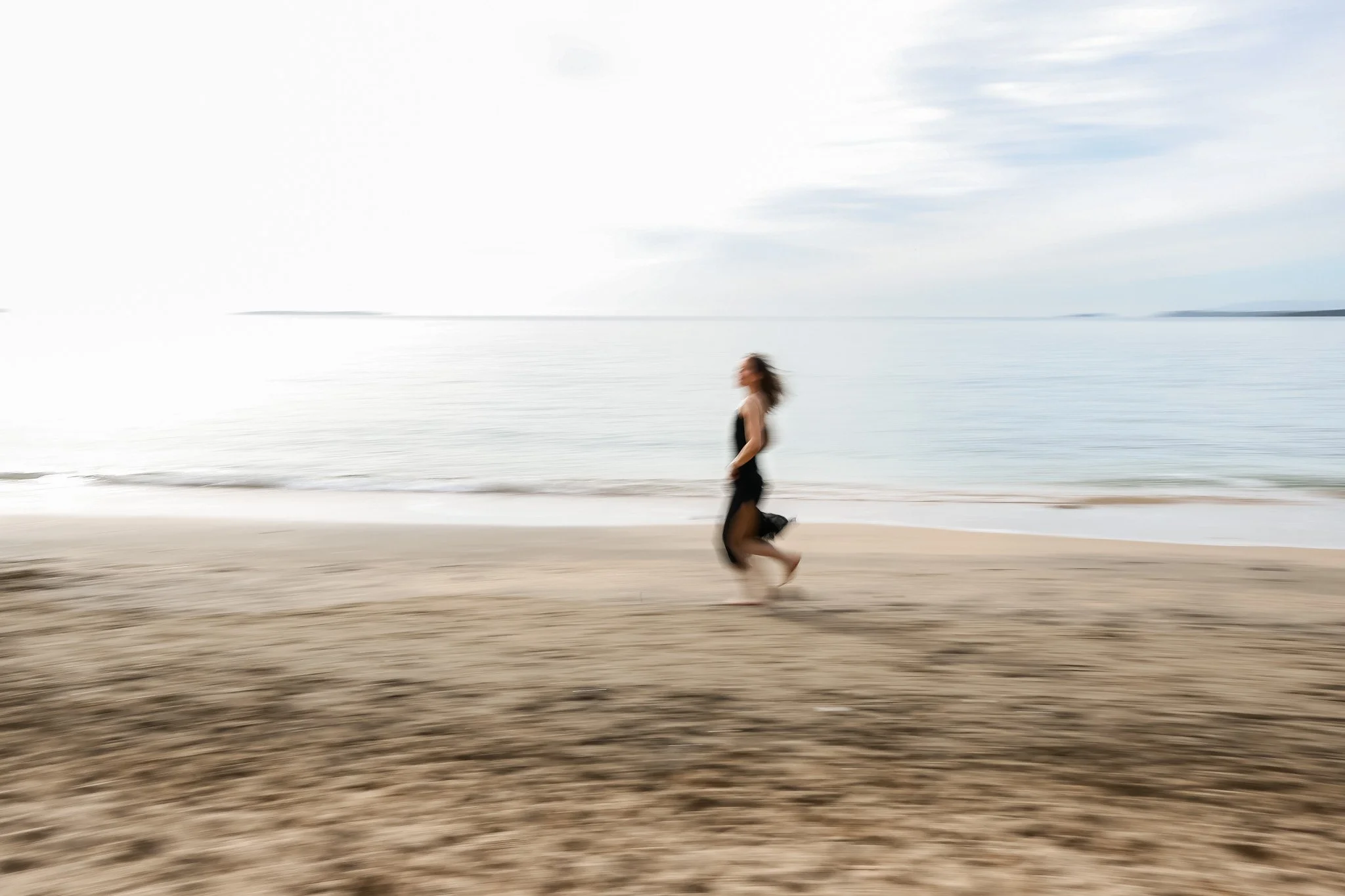 A woman running on a beach with the ocean and sky in the background, the image is blurred