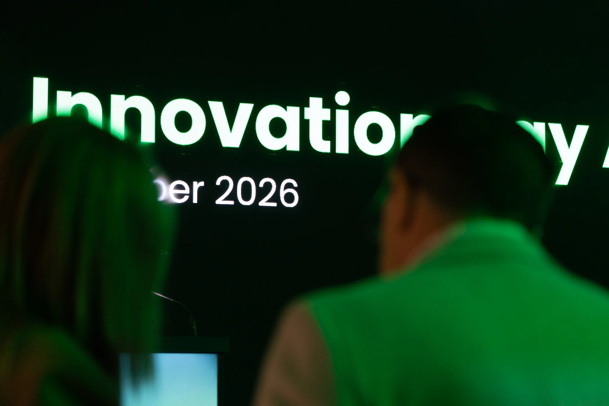 Close-up of a digital screen with the word 'Innovation' in green illuminated letters, and people in the foreground.