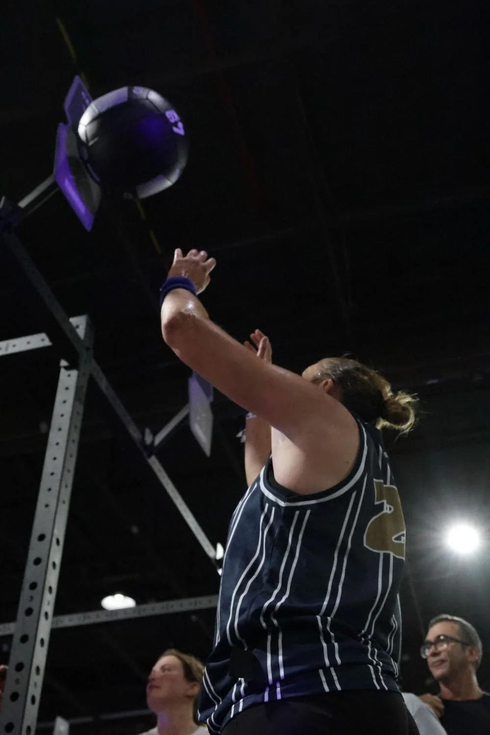 A woman in athletic attire jumps to block a volleyball during a game in an indoor gym.
