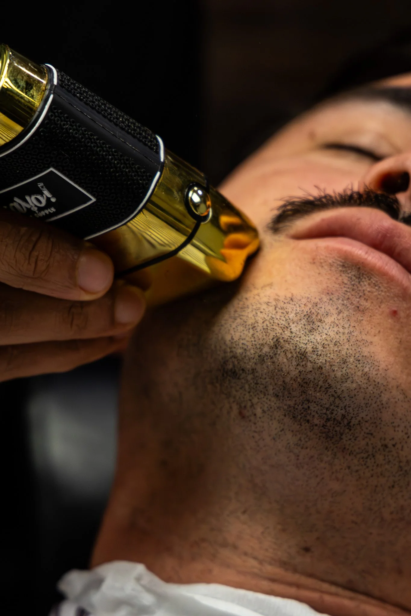 A man with a beard and closed eyes is resting his head against a gold-colored object, possibly a bottle, held close to his face.