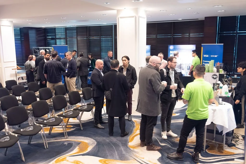 People attending a professional event or conference in a well-lit room with vendor booths and rows of empty chairs.