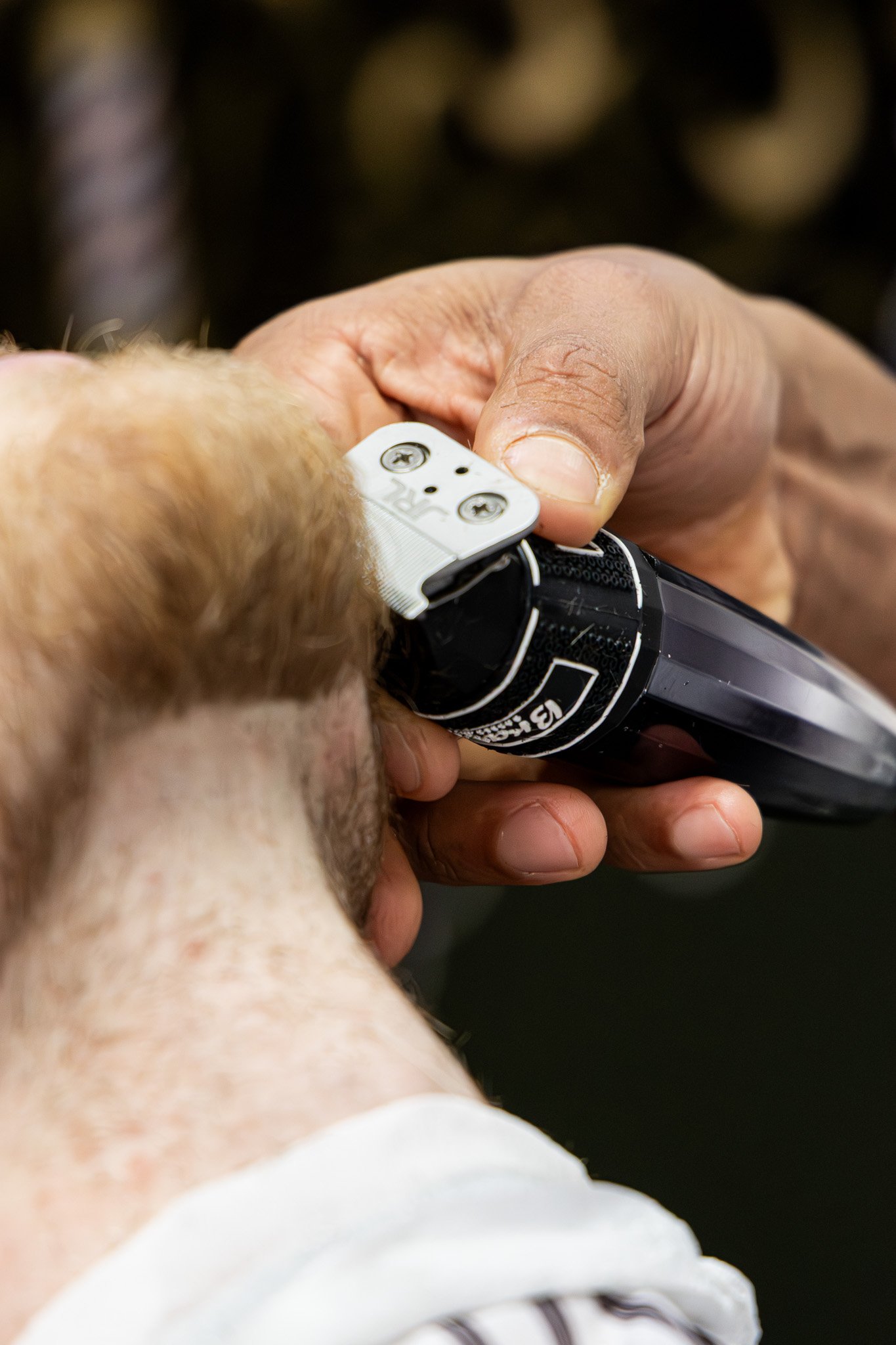 Close-up of a person with pale skin and aging hands holding an electric shaver. The background is dark.
