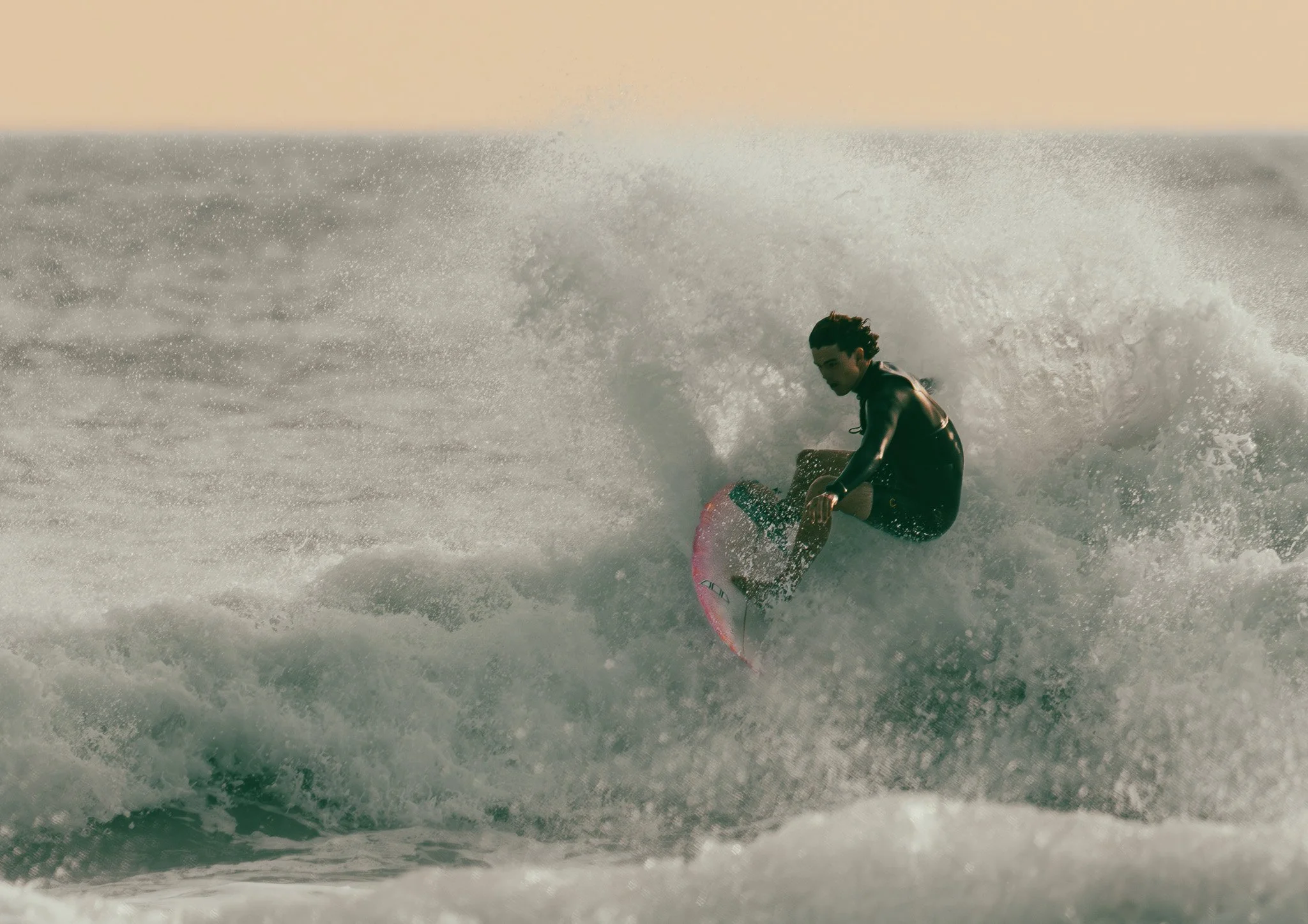 A person riding a surfboard on a wave in the ocean at sunset.