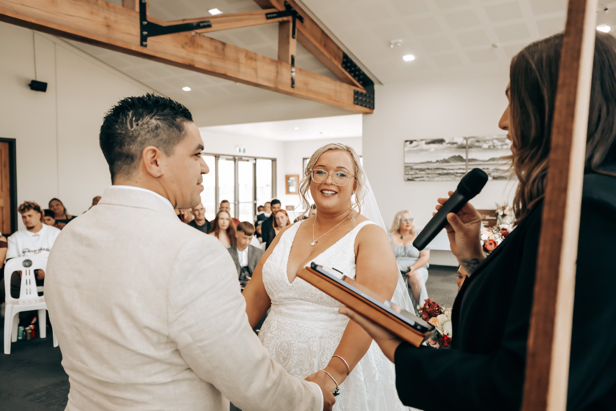 A wedding ceremony with a bride and groom exchanging vows, surrounded by guests in a bright indoor setting.