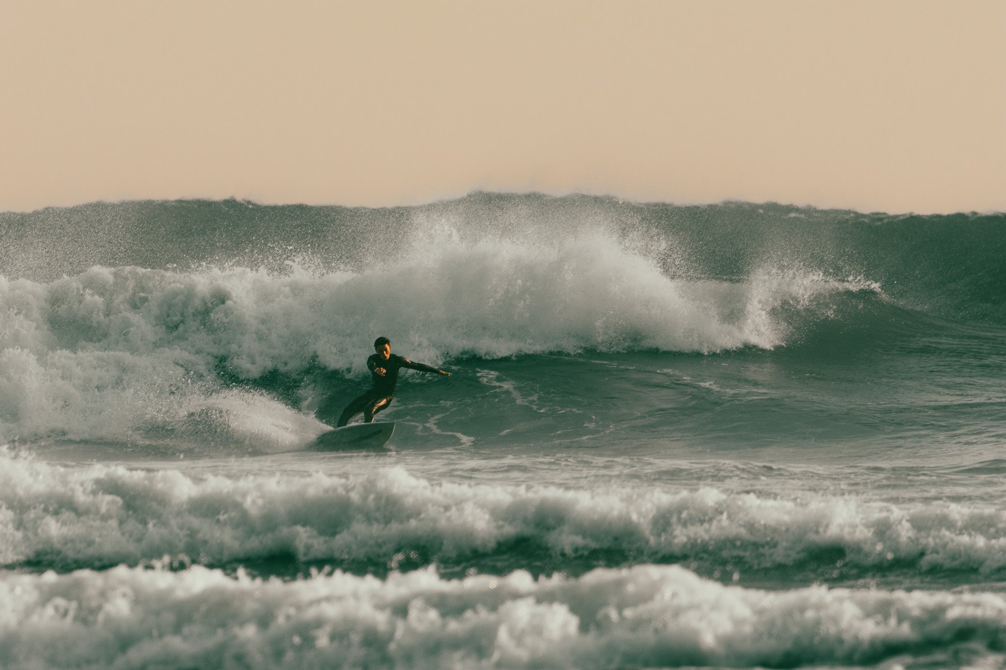 Surfer riding a wave in the ocean during sunset.