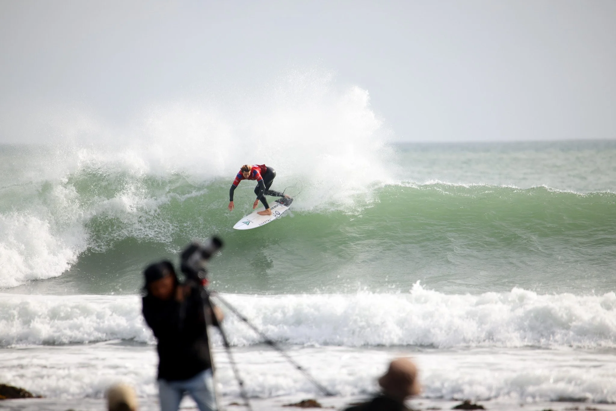 A person surfing on a wave in the ocean with a crowd watching from the shore.