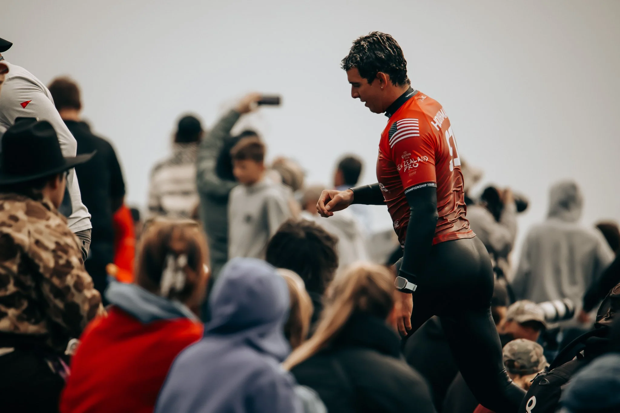 A cyclist in a red jersey standing among seated spectators during a race.